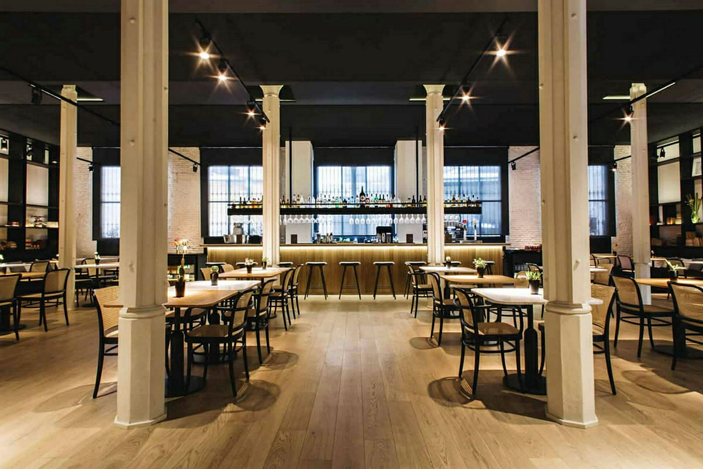 En elegant restaurang med bord och stolar samt en välbelyst bardisk i bakgrunden. (AI-genererad text)