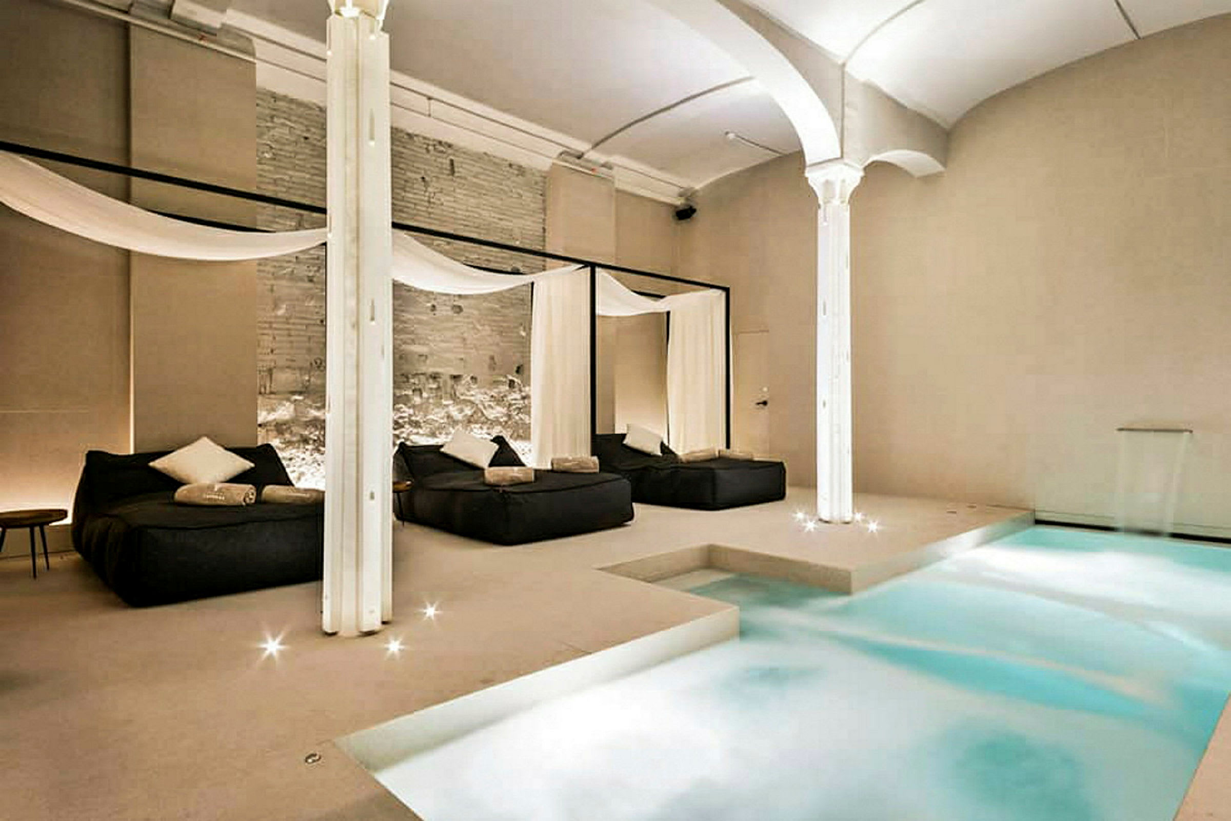 Ett elegant inomhusspa med en pool och avkopplingsområden med sängar och dekorativa draperier. (AI-genererad text)