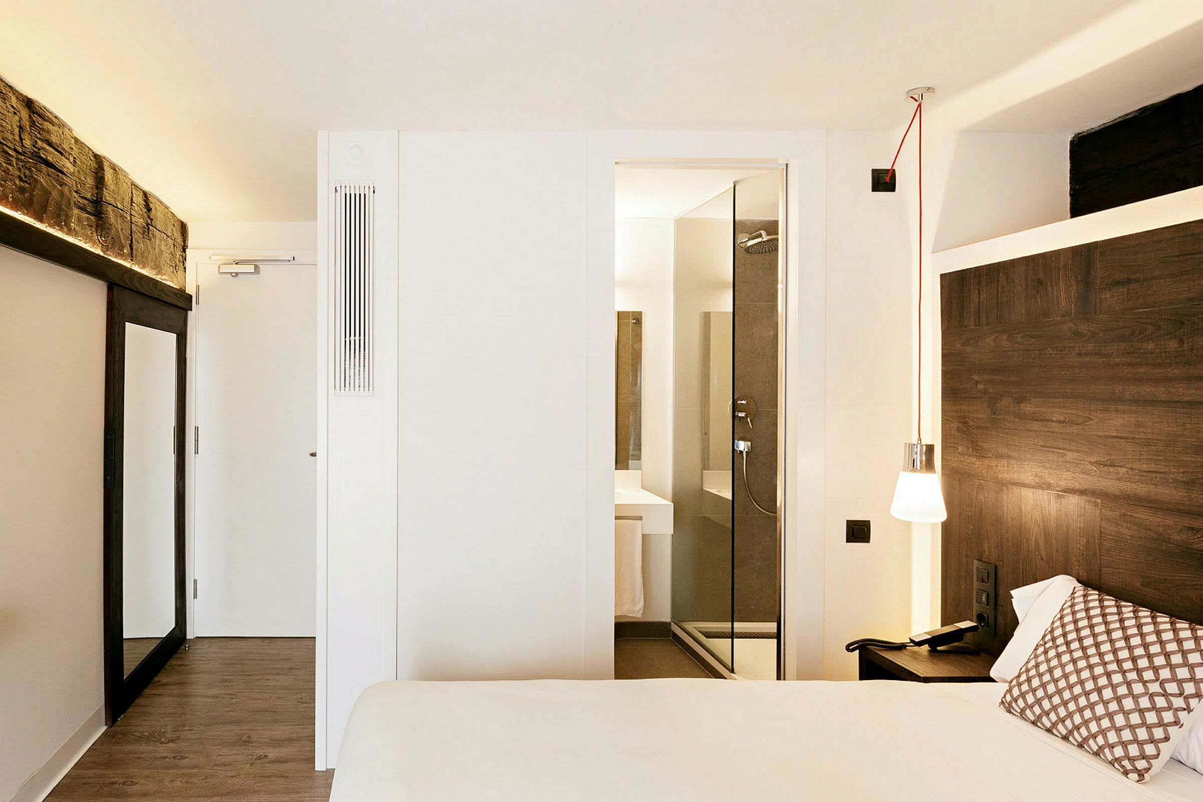 Ett modernt hotellrum med en dubbelsäng, ett träklätt huvudgavel och fönster som leder till ett badrum med glasdörr. (AI-genererad text)