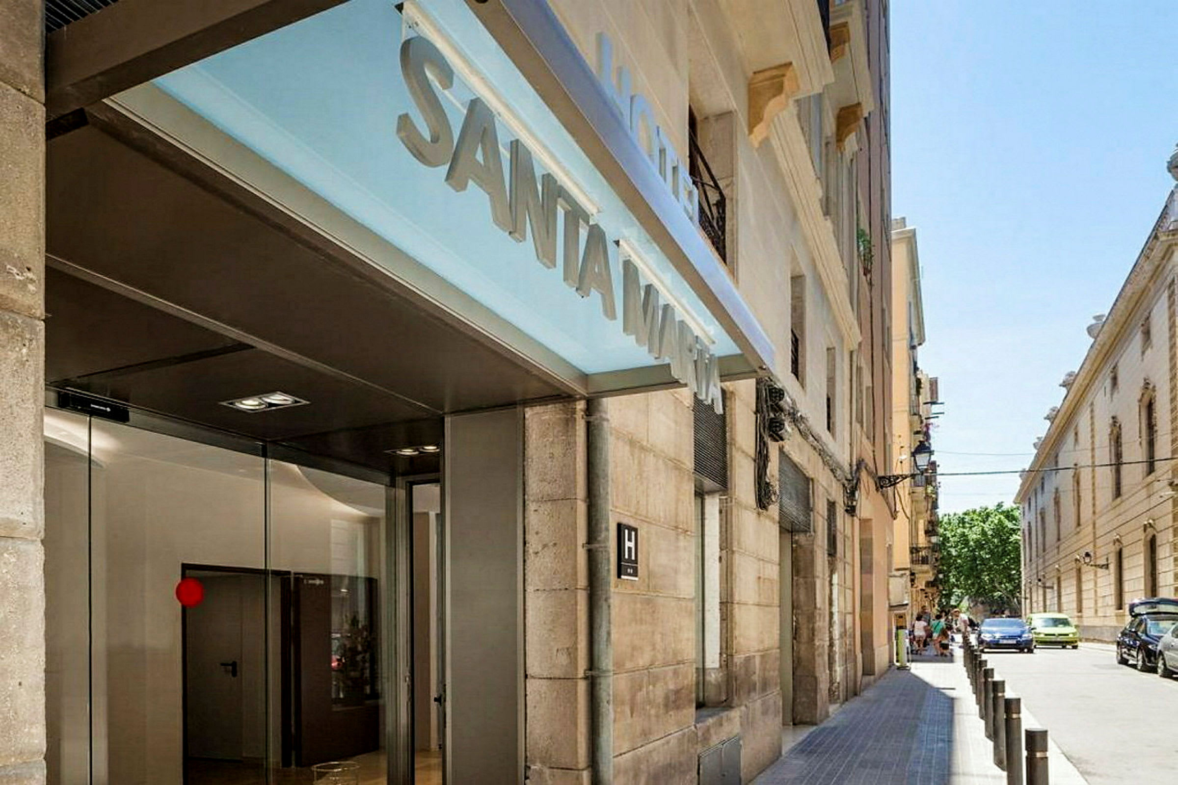 Entrén till ett hotell med texten "Santa Marta" på en skylt och en gata synlig i bakgrunden. (AI-genererad text)