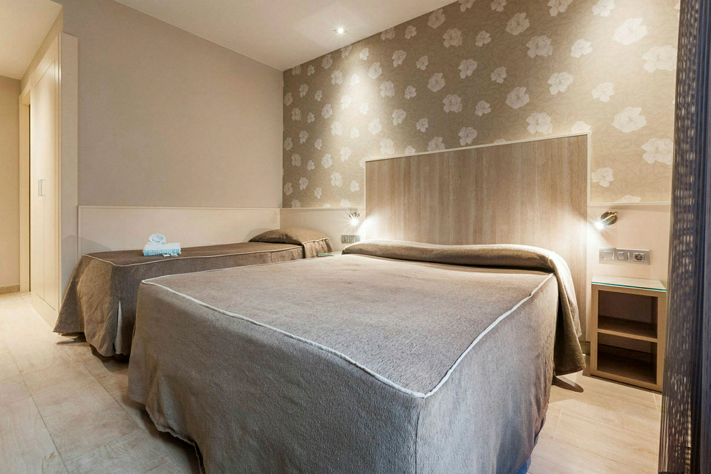 Ett hotellrum med två sängar, beige väggar och blommigt tapetmönster bakom huvudgaveln. (AI-genererad text)