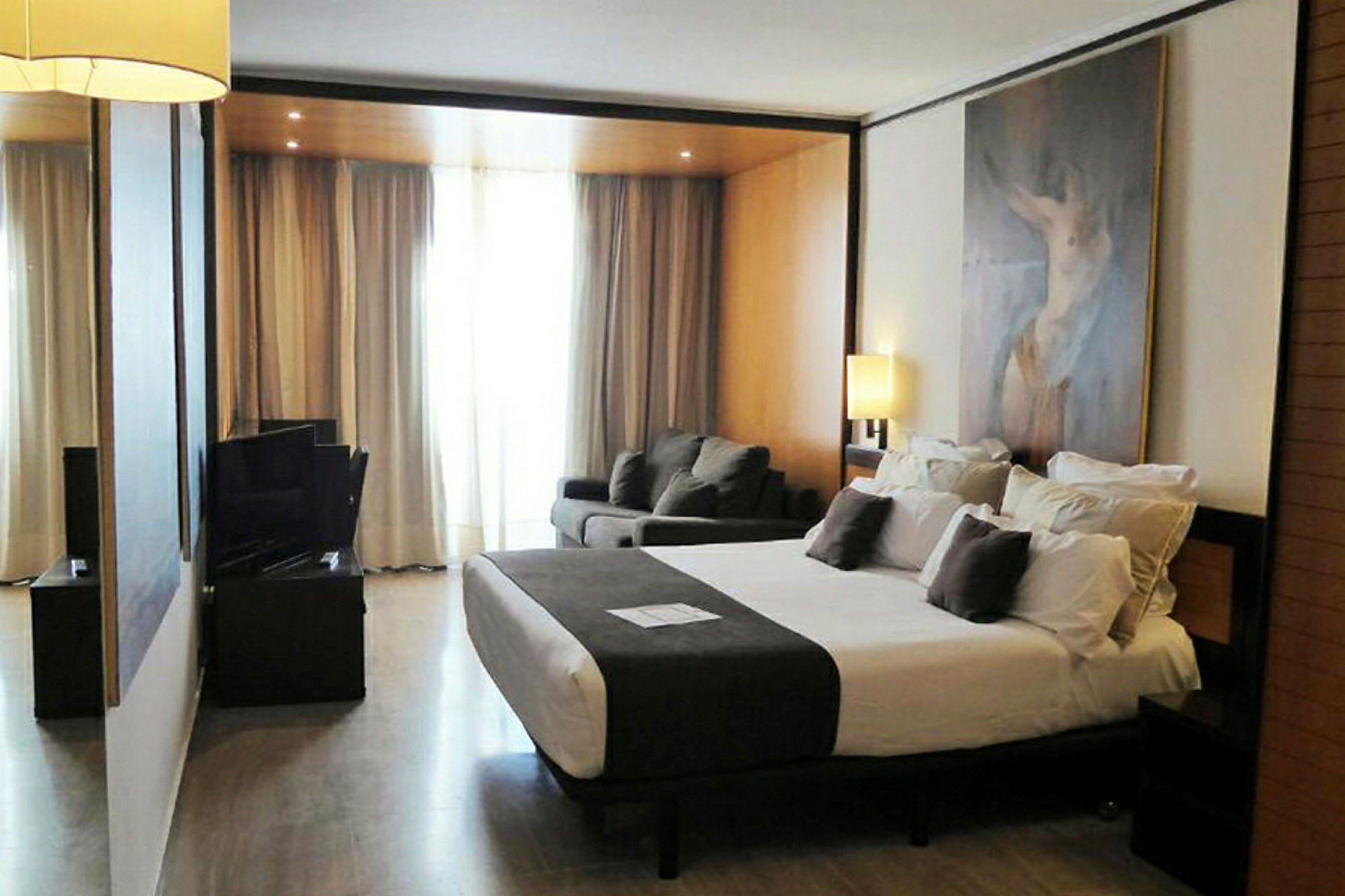 Ett hotellrum med stor säng, soffgrupp och lampor, samt en målning på väggen. (AI-genererad text)