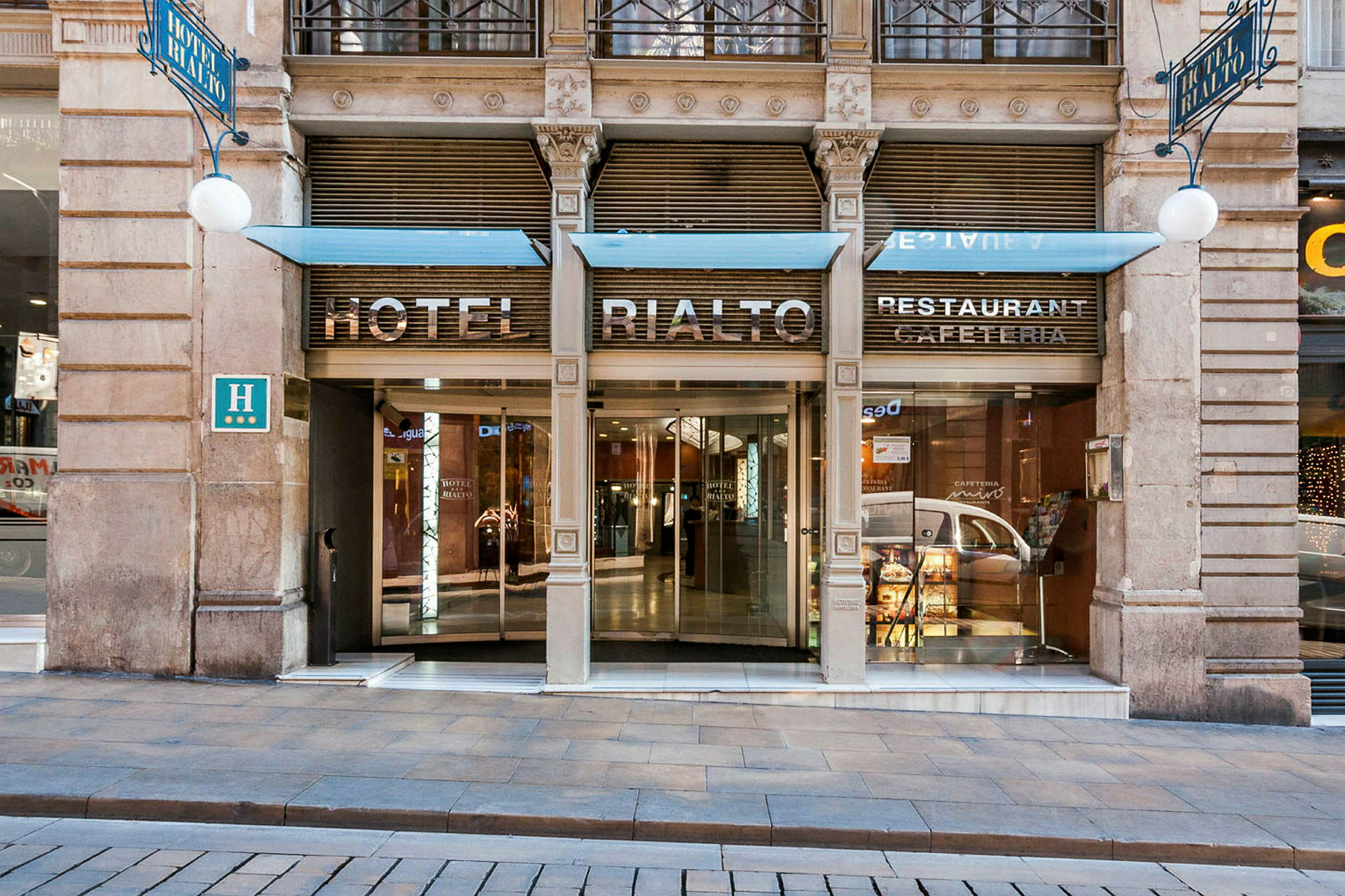 Entré till ett hotell med texten "Hotel Rialto" ovanför dörrarna. (AI-genererad text)