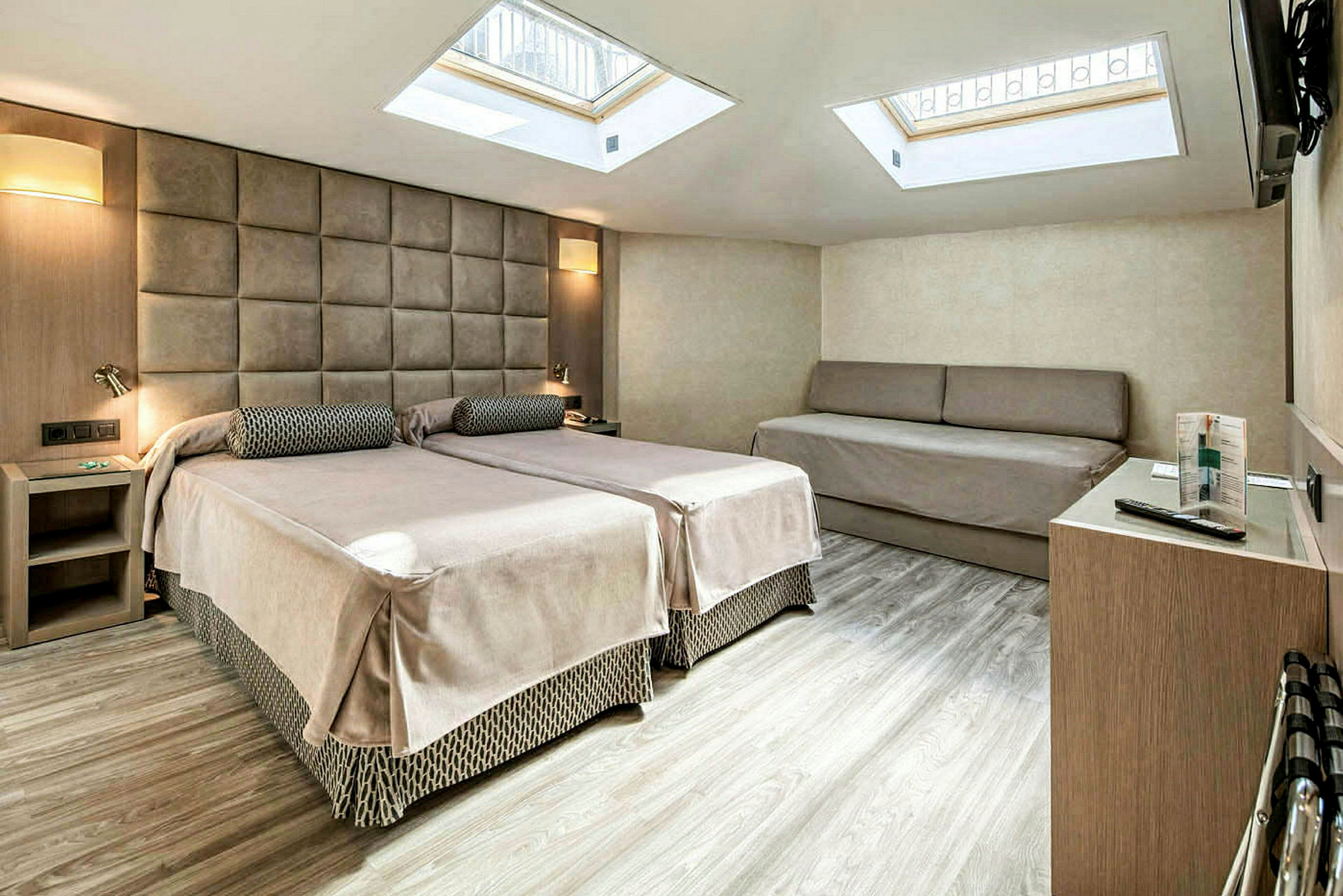 Ett hotellrum med två enkelsängar, en soffa och takfönster. (AI-genererad text)