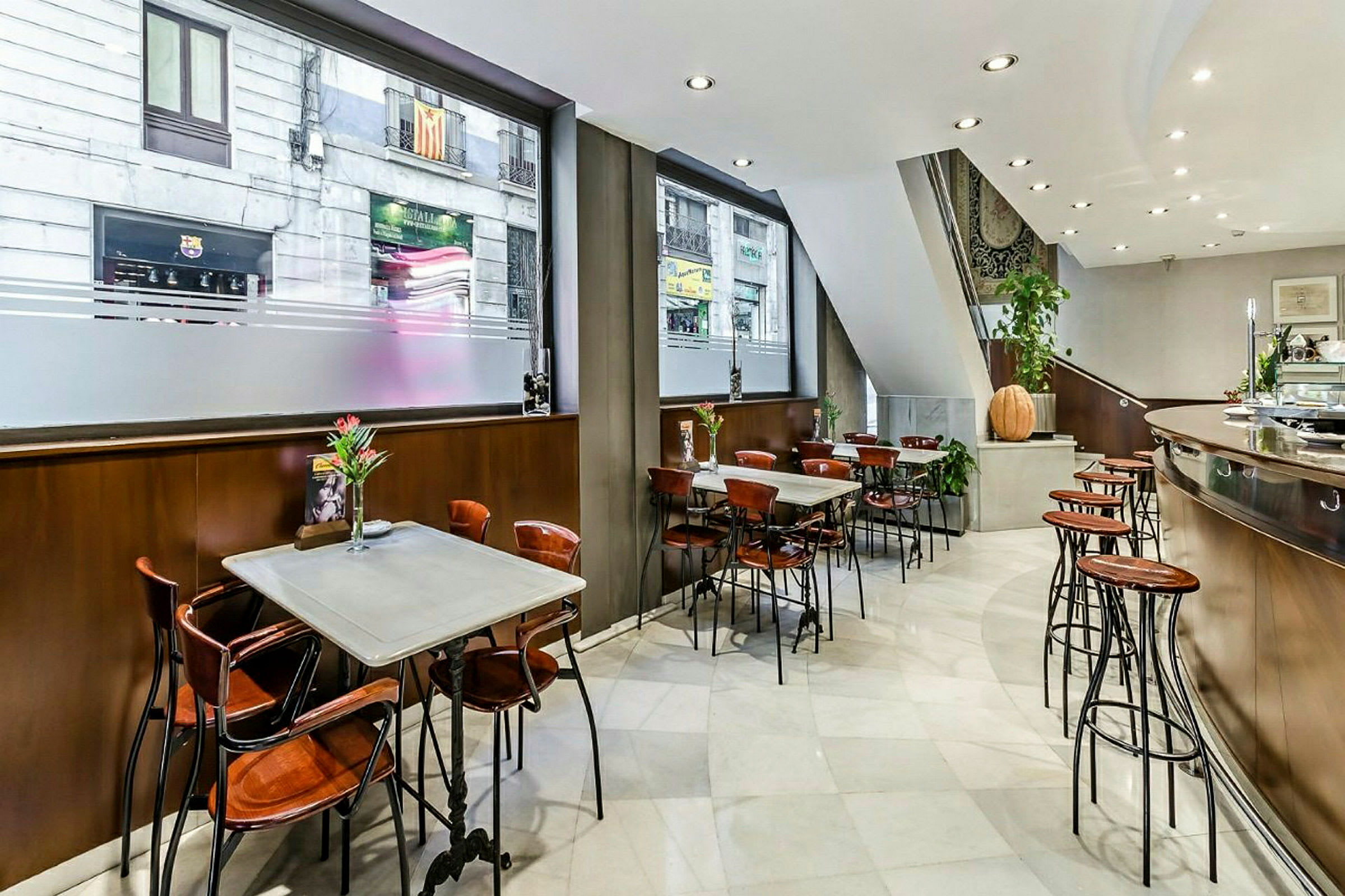 Ett café med vita bord, trästolar och barstolar längs en disk. Stora fönster mot gatan. (AI-genererad text)