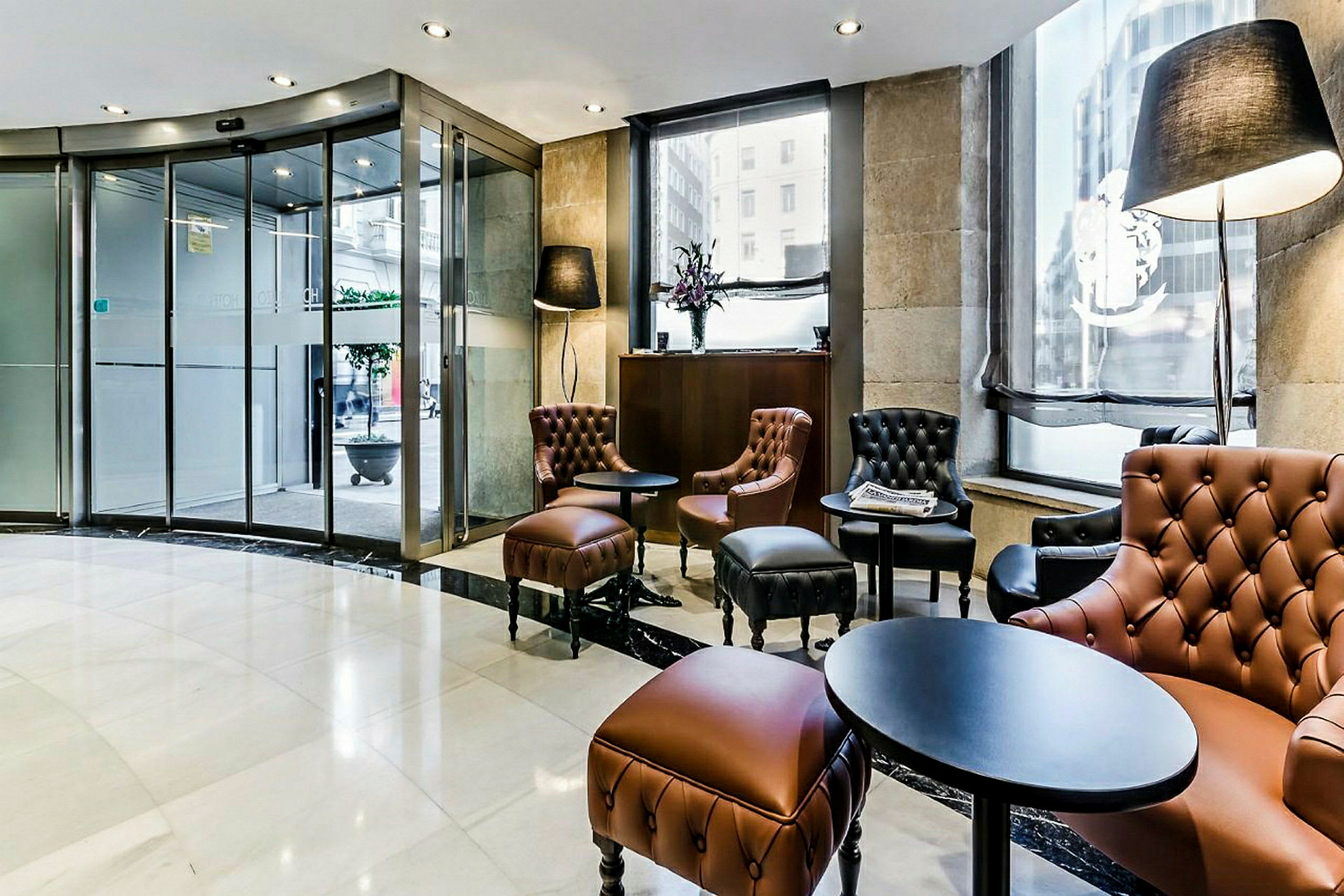 Bild av en hotelllobby med läderfåtöljer och små bord nära en glasdörr. (AI-genererad text)