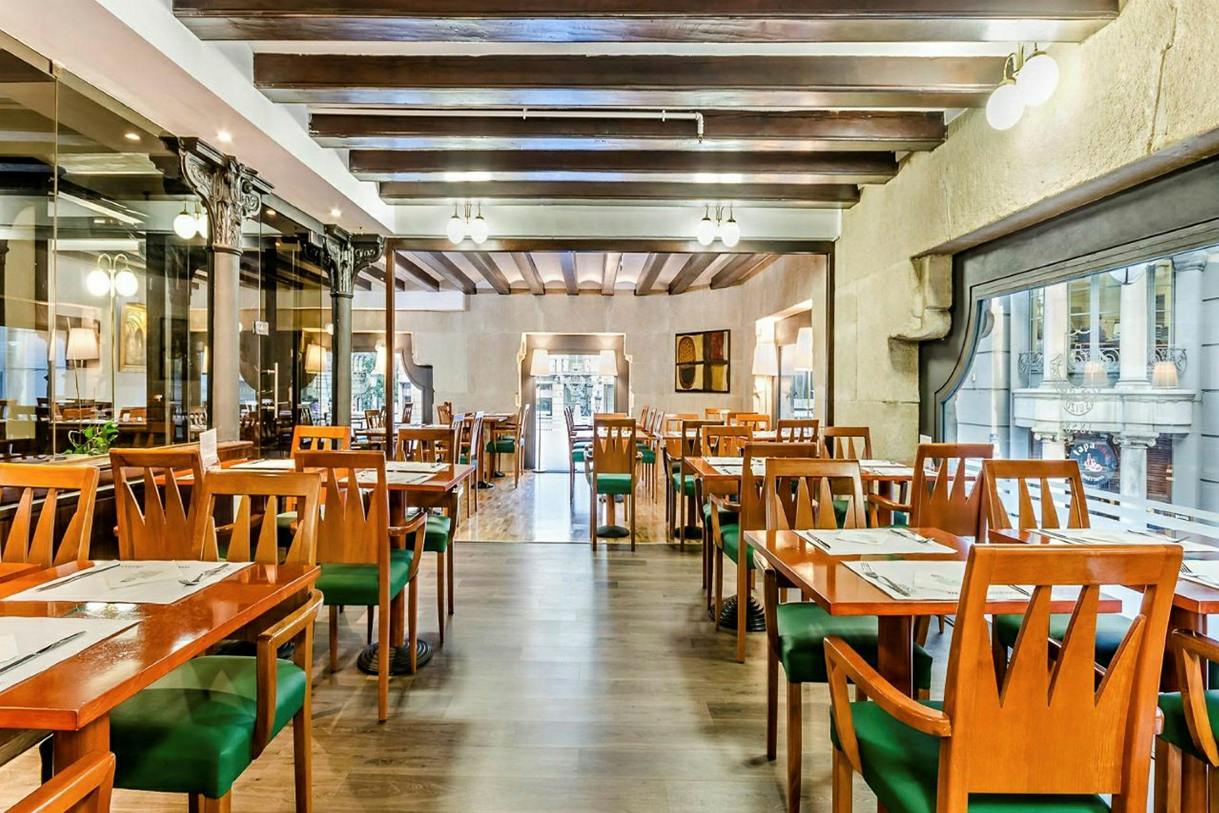 En interiör av en restaurang med tomma bord och stolar, träbjälkar i taket och stora fönster mot en gata. (AI-genererad text)