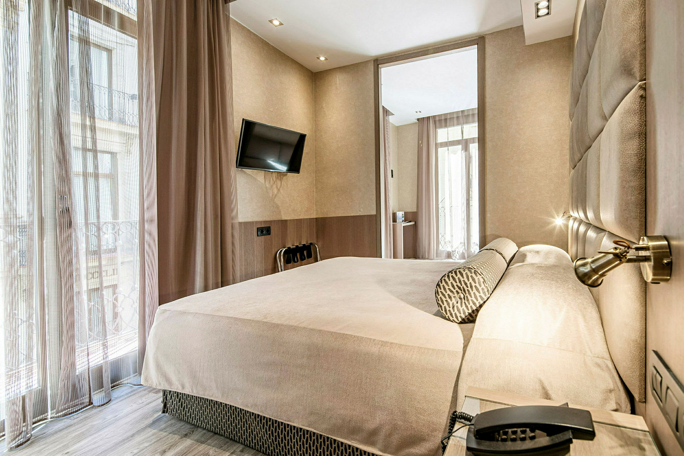 Ett hotellrum med en stor säng, ett väggmonterat tv och stora fönster med gardiner. (AI-genererad text)