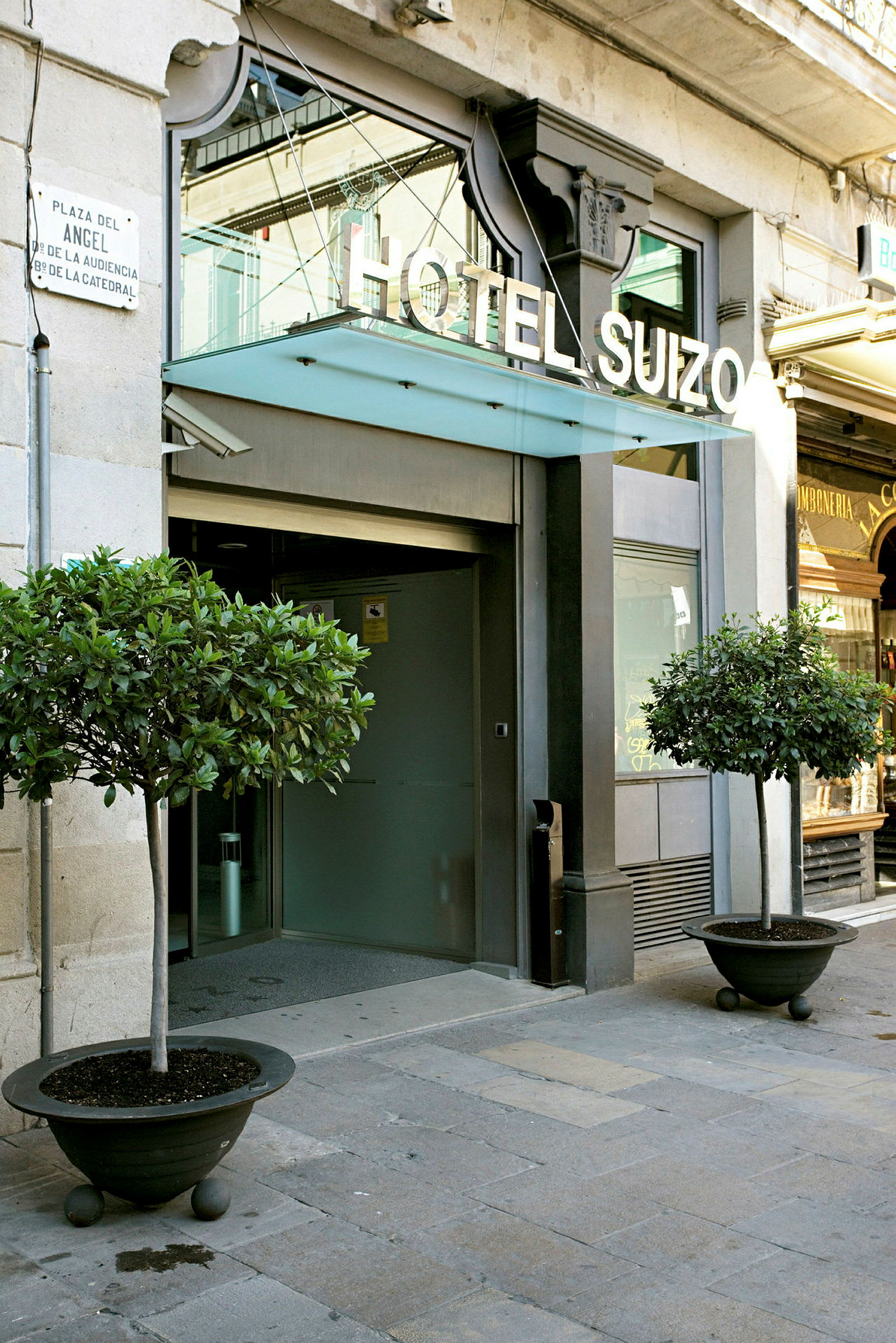 Entré till Hotel Suizo med två prydnadsträd i stora krukor på vardera sidan. (AI-genererad text)