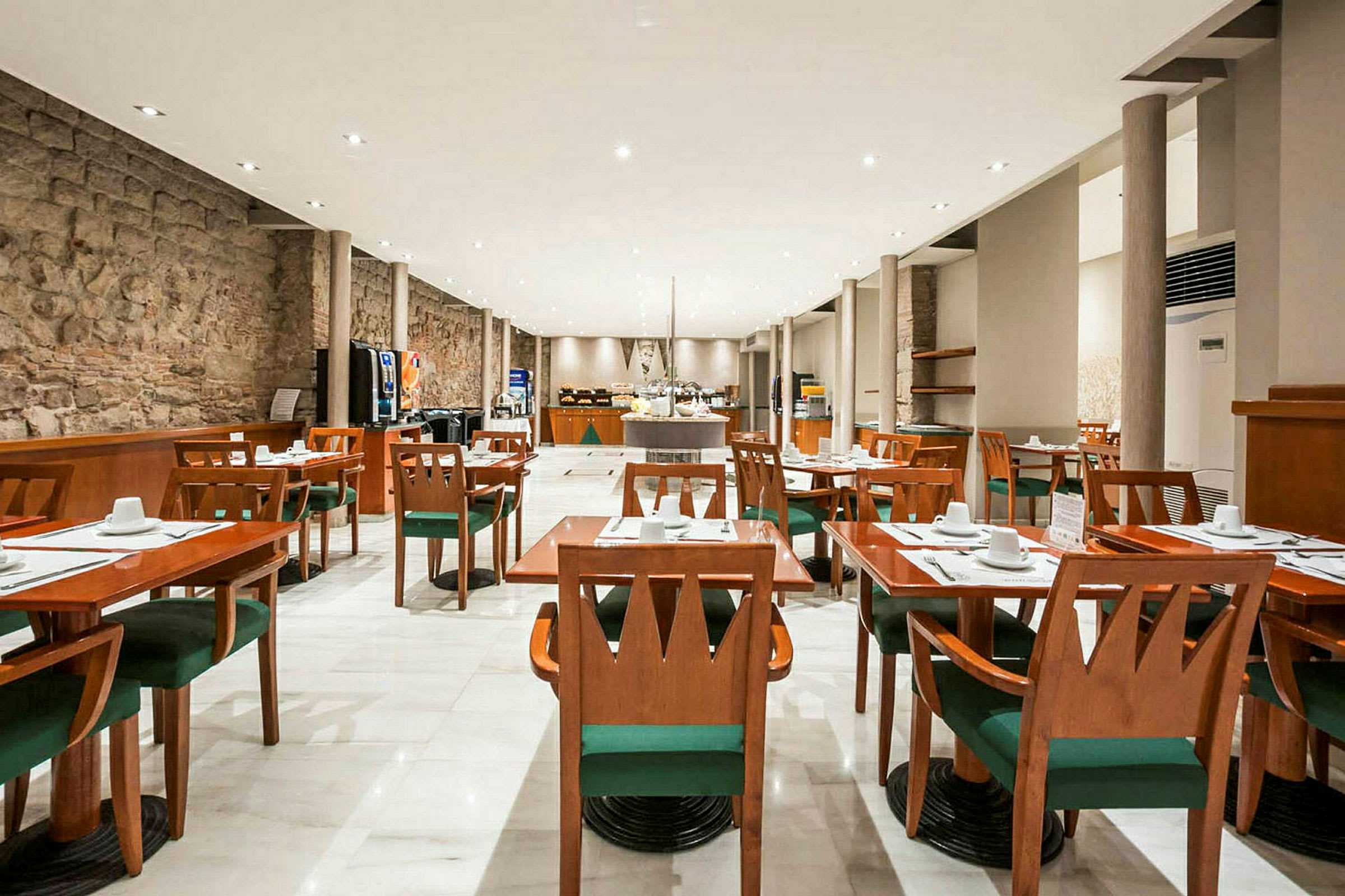 Ett rymligt restaurangutrymme med trämöbler, vita dukar, gröna stolar och en modern inredning. (AI-genererad text)