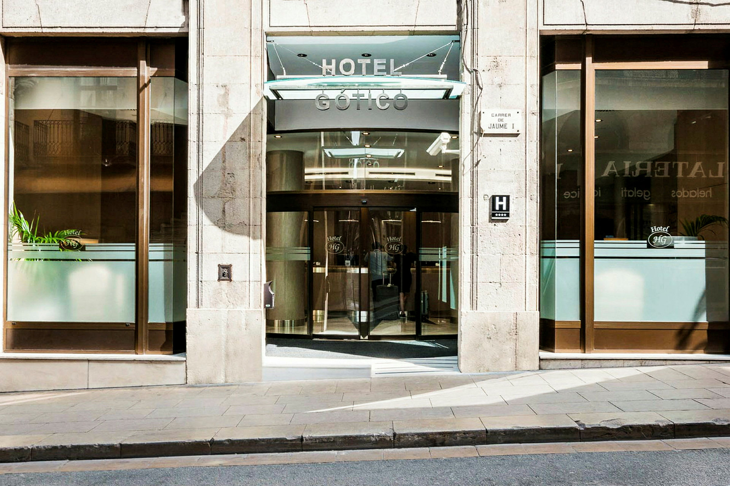 Entré till ett hotell med glasdörrar och ett hotellnamn synligt ovanför. (AI-genererad text)