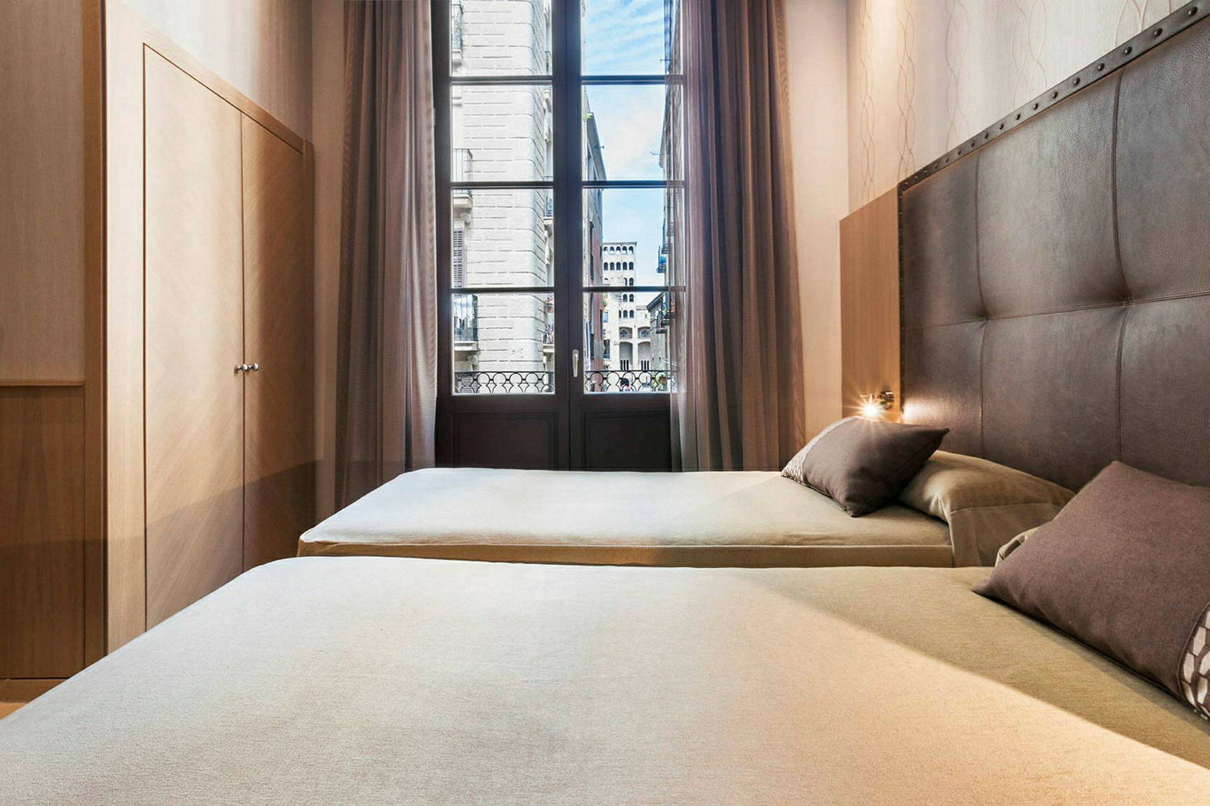Ett hotellrum med två sängar, en garderob och ett stort fönster med utsikt mot en stad. (AI-genererad text)
