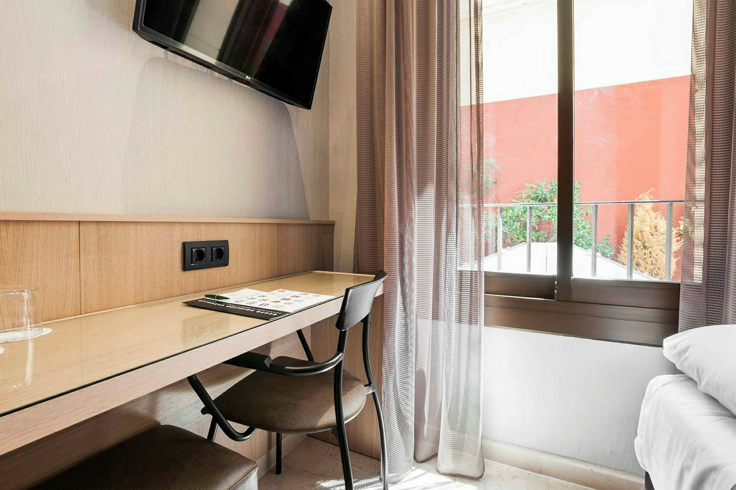 Skrivbord i ett hotellrum med stol, skrivmaterial, TV på väggen och ett fönster i bakgrunden. (AI-genererad text)