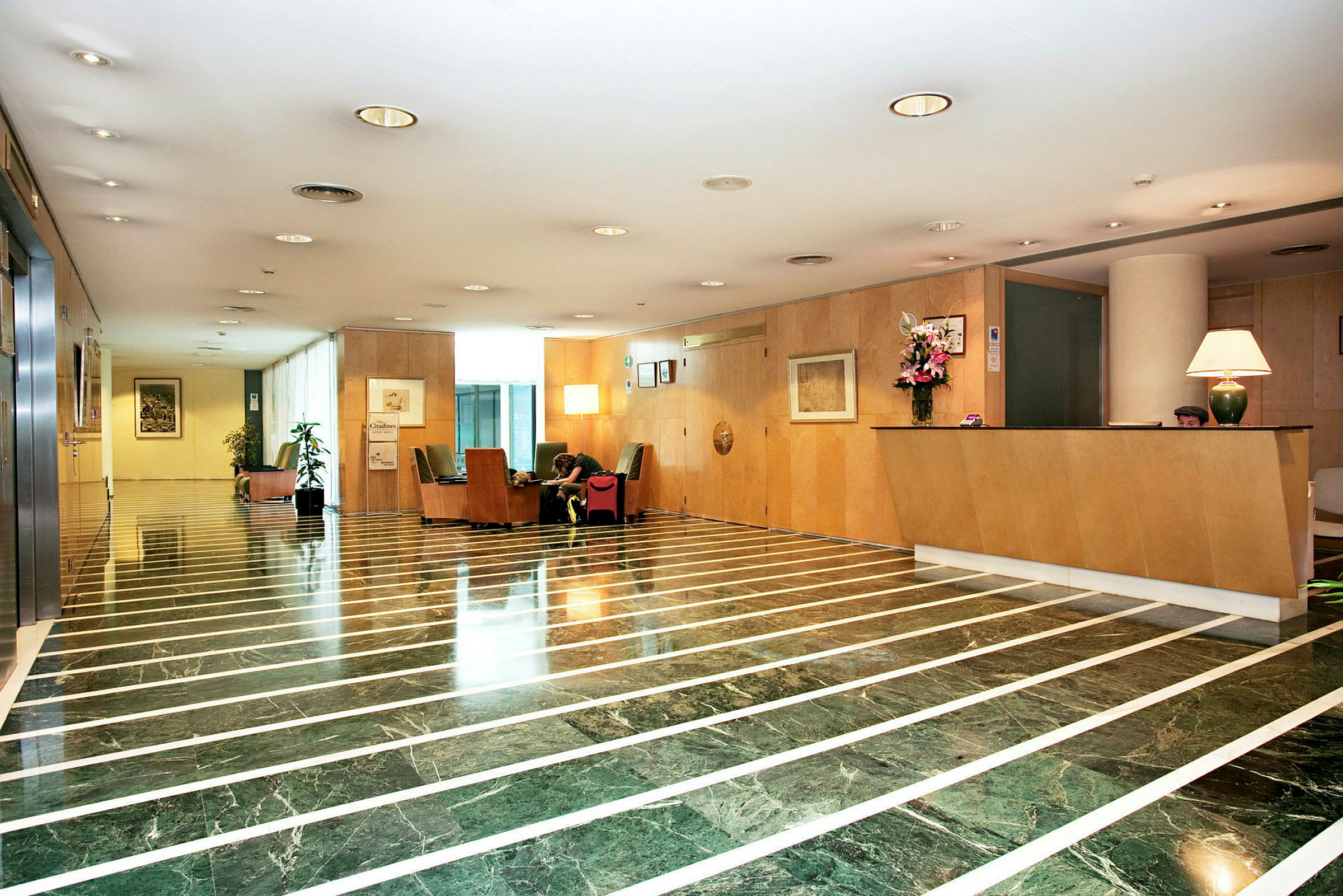 Ett ljust och öppet hotellobbyområde med marmorgolv, en reception och sittplatser. (AI-genererad text)