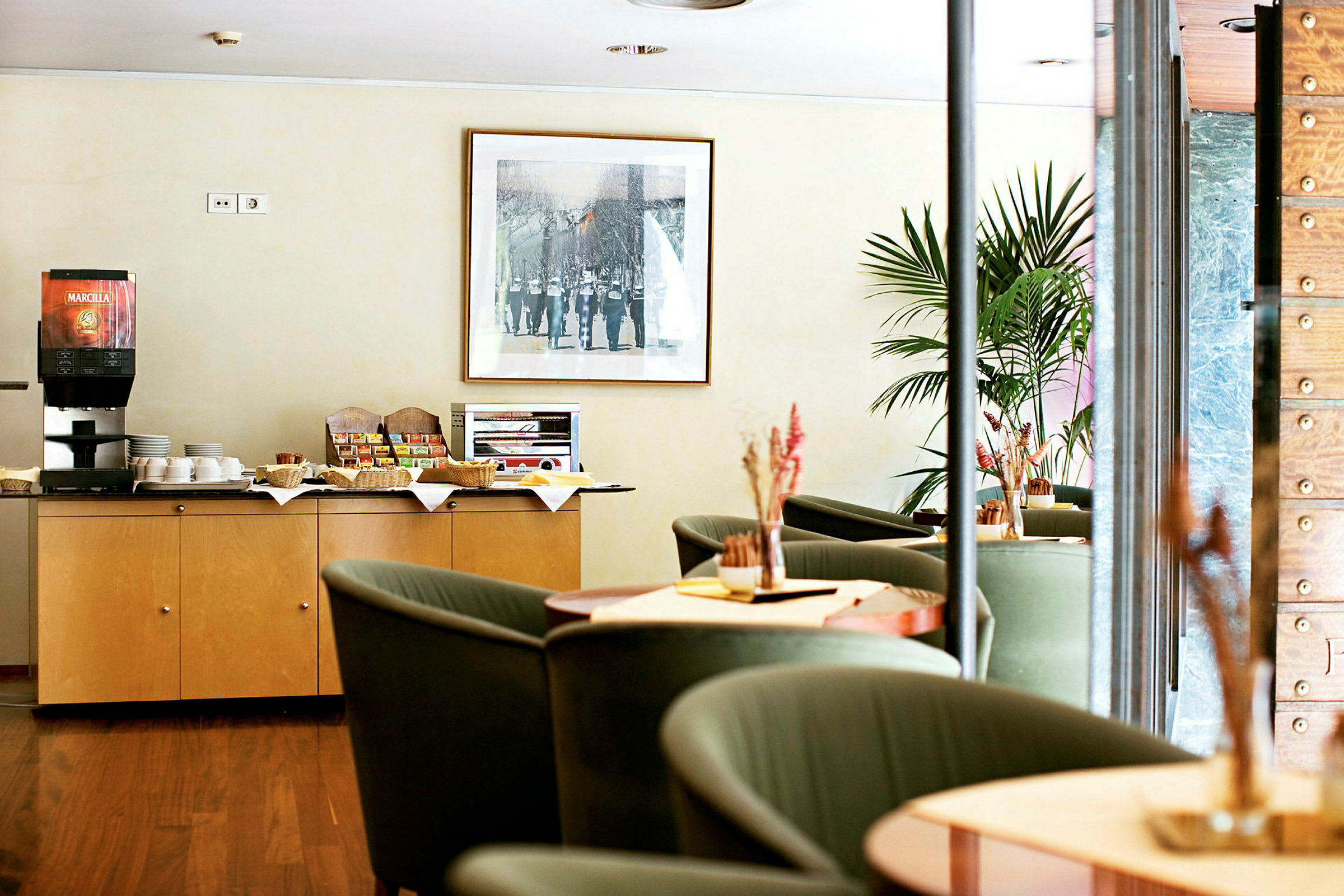 En kaffestation och sittgrupp i ett hotell eller kafé. En koppautomat och mellanmål finns på ett skåp. (AI-genererad text)