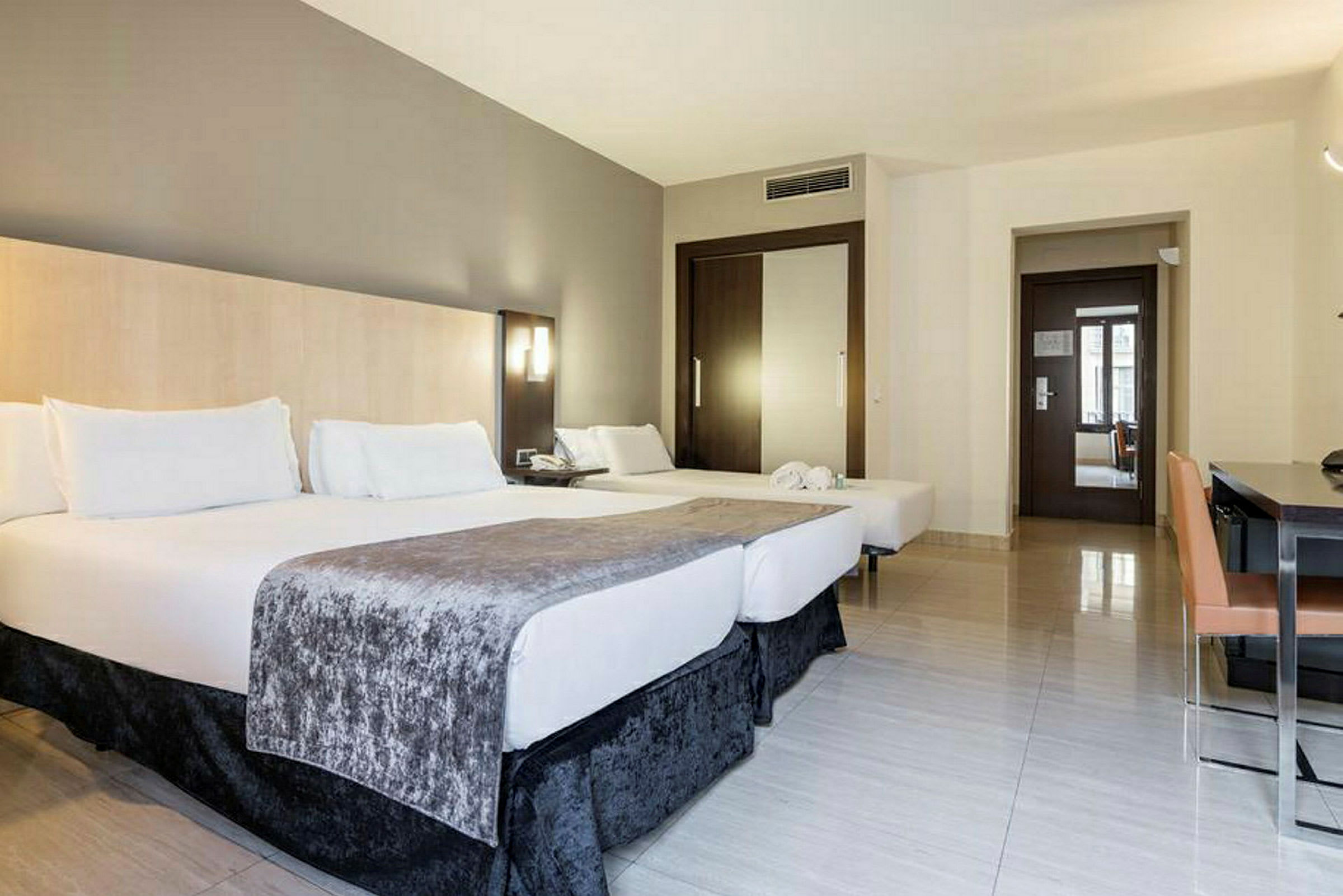 Hotellrum med två dubbelsängar, skrivbord och stol, samt en dörr till badrummet. (AI-genererad text)