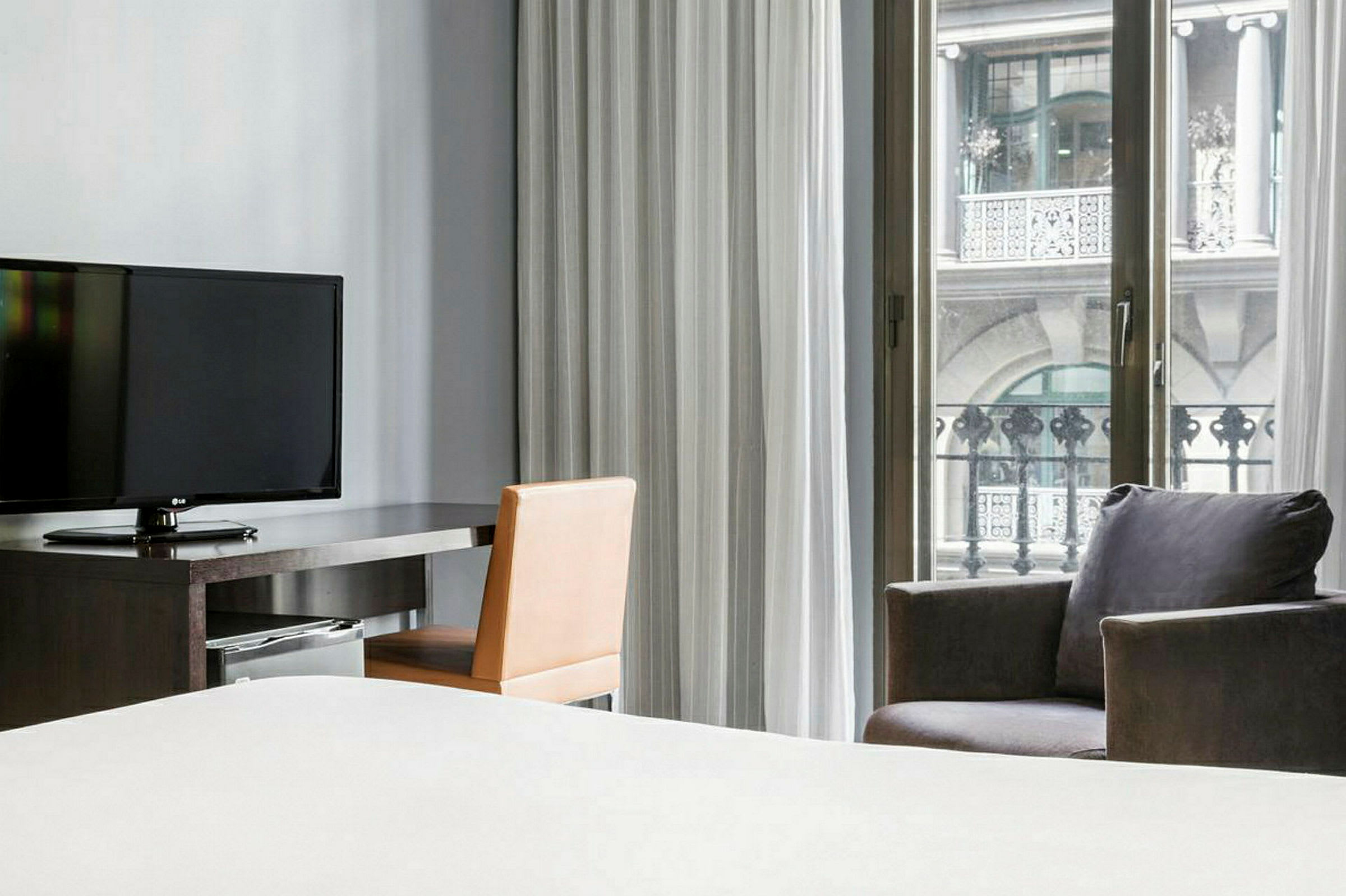 Ett hotellrum med tv, arbetsbord, och ett fönster med utsikt över en balkong. (AI-genererad text)