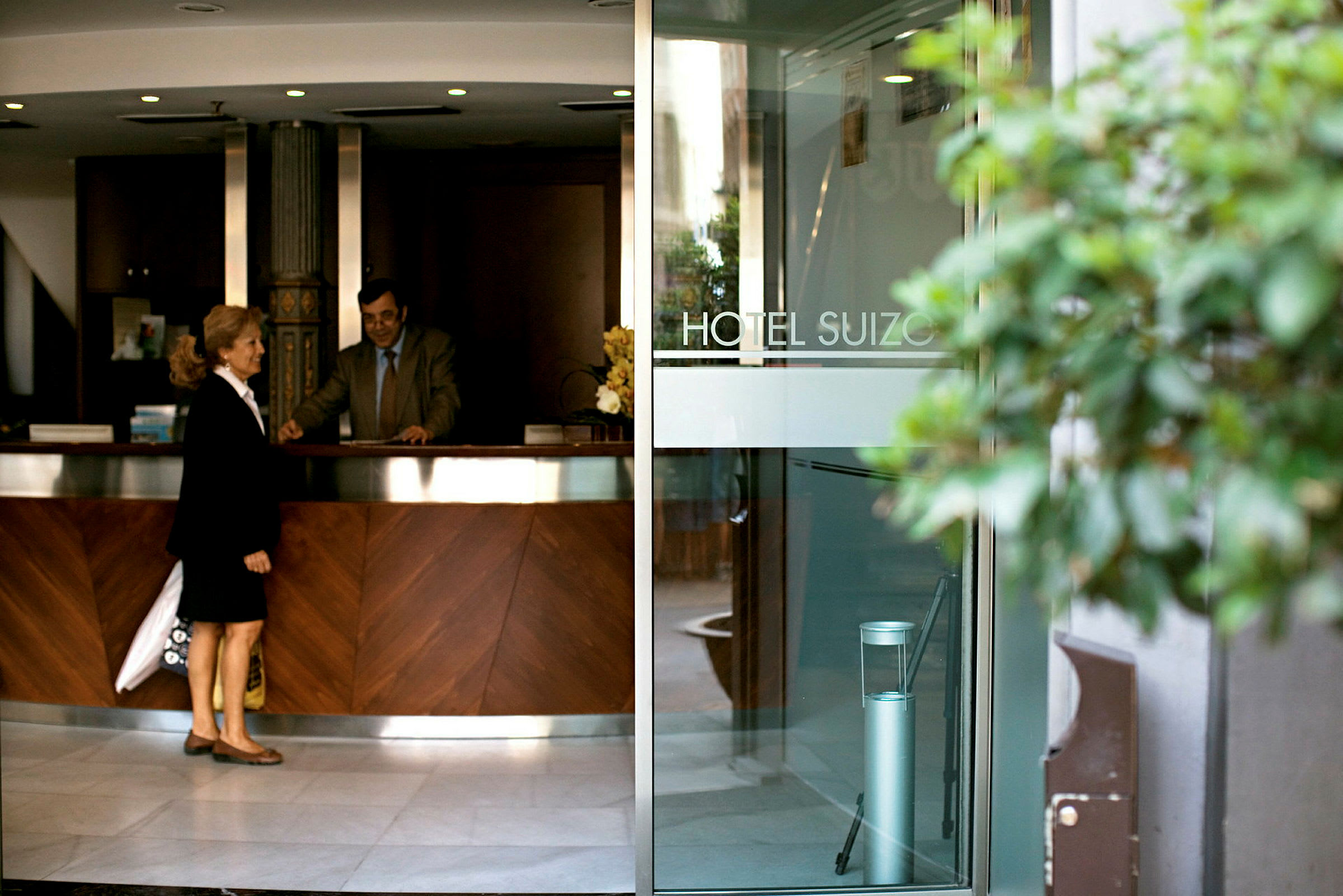 En bild av ingången och receptionen på Hotel Suizo. En receptionist och en gäst står vid disken. (AI-genererad text)
