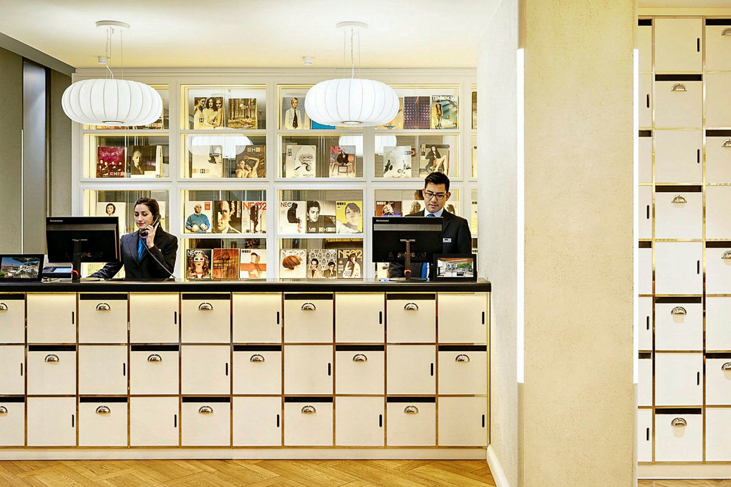 Reception med vita skåp och dekorativ belysning, bakom receptionsdisken finns en vägghylla med tidningar och magasin. (AI-genererad text)