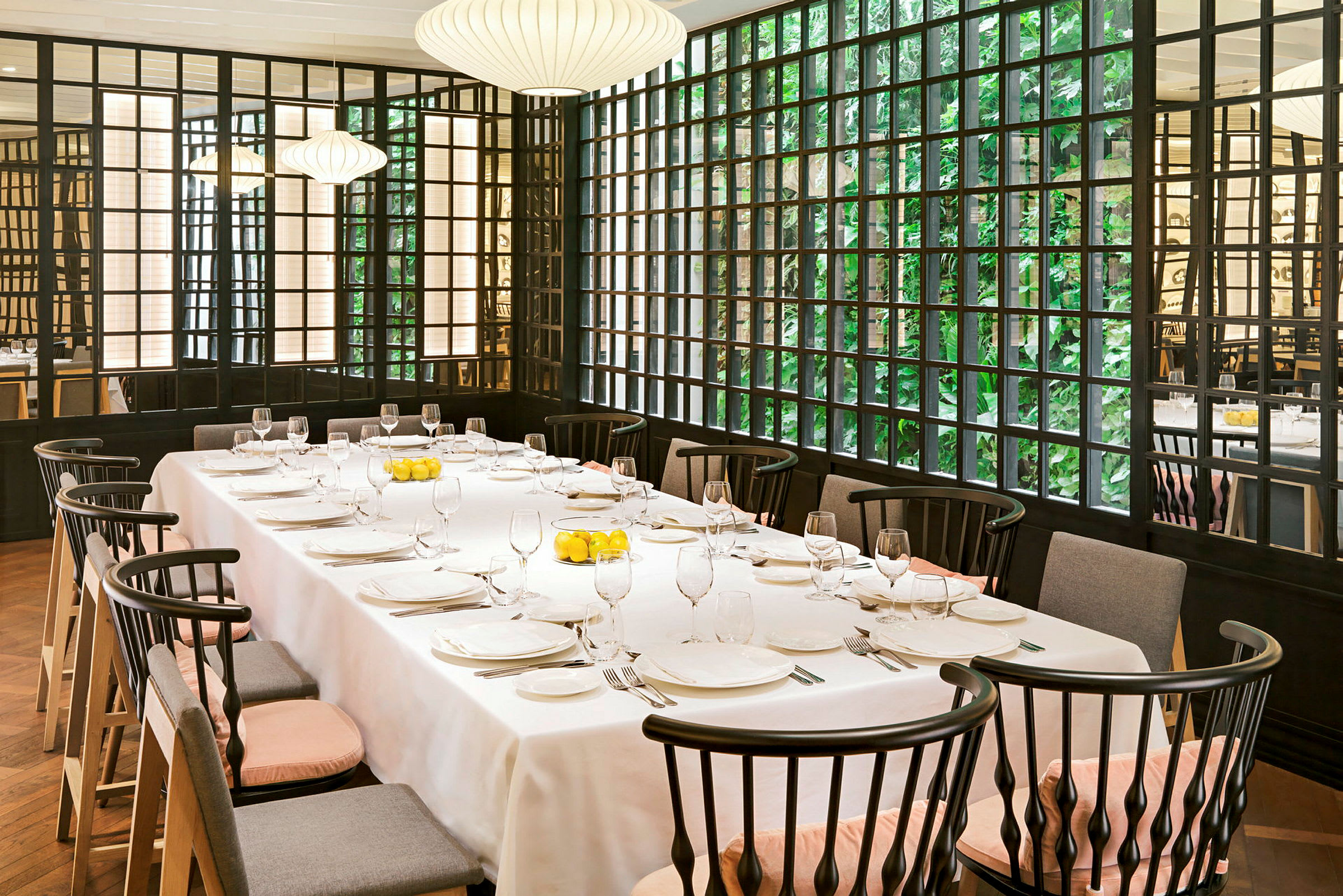 Ett uppdukat bord i en restaurang med eleganta stolar och stora fönster med grönska utanför. (AI-genererad text)