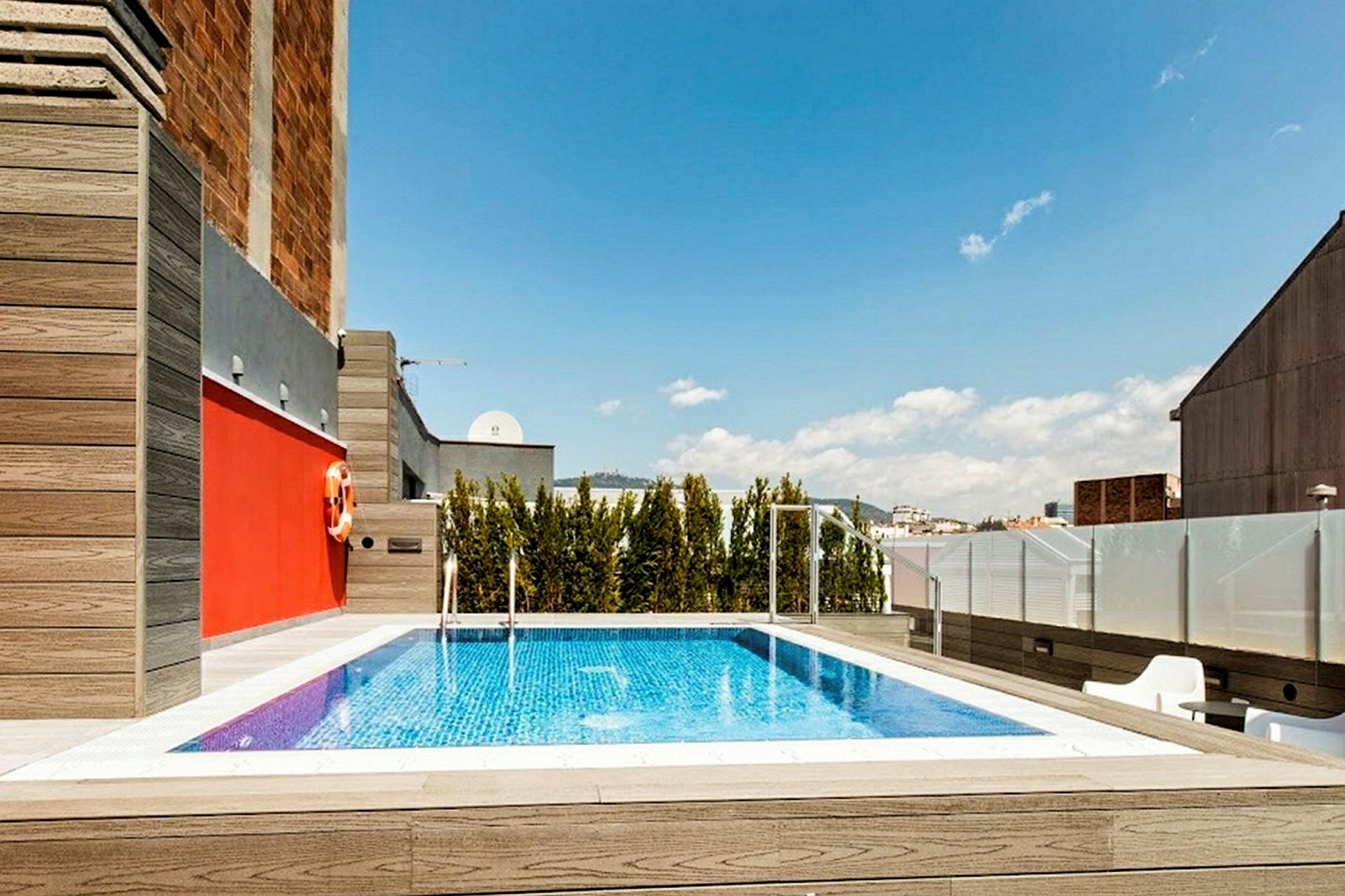 En pool på en takterrass med träd och byggnader i bakgrunden. (AI-genererad text)