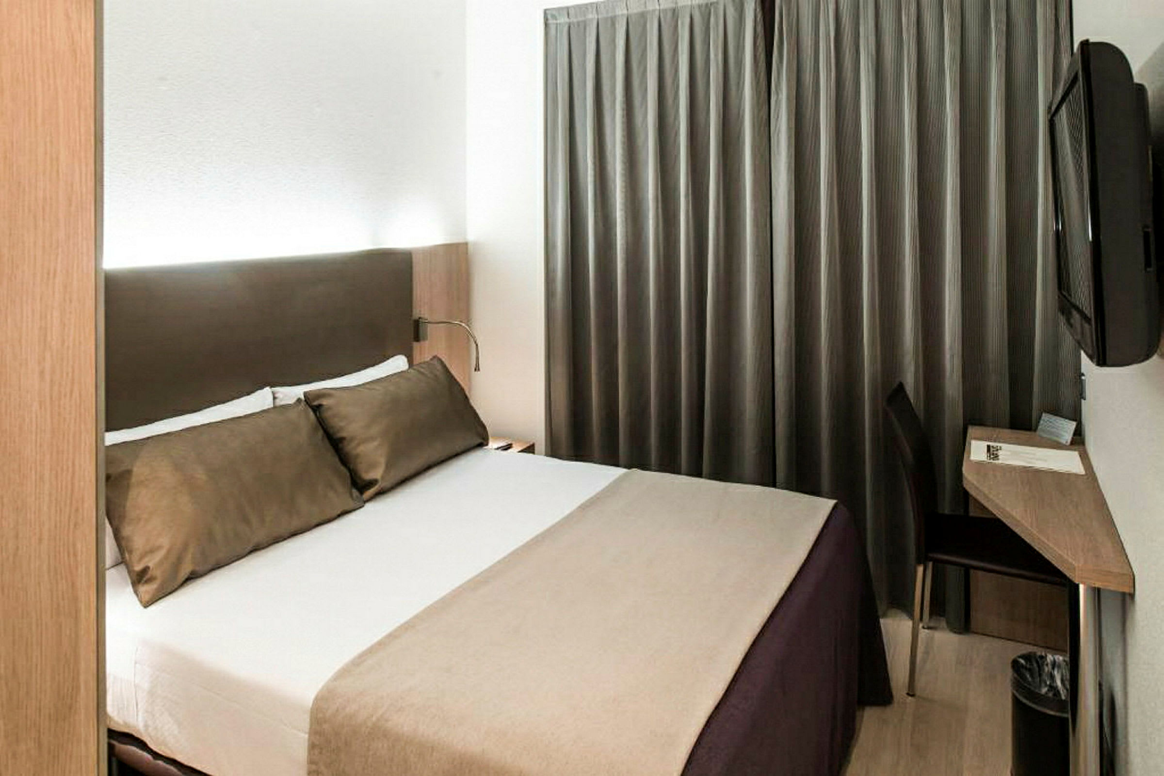 Ett hotellrum med en stor säng, mörka gardiner, ett skrivbord och en väggmonterad TV. (AI-genererad text)