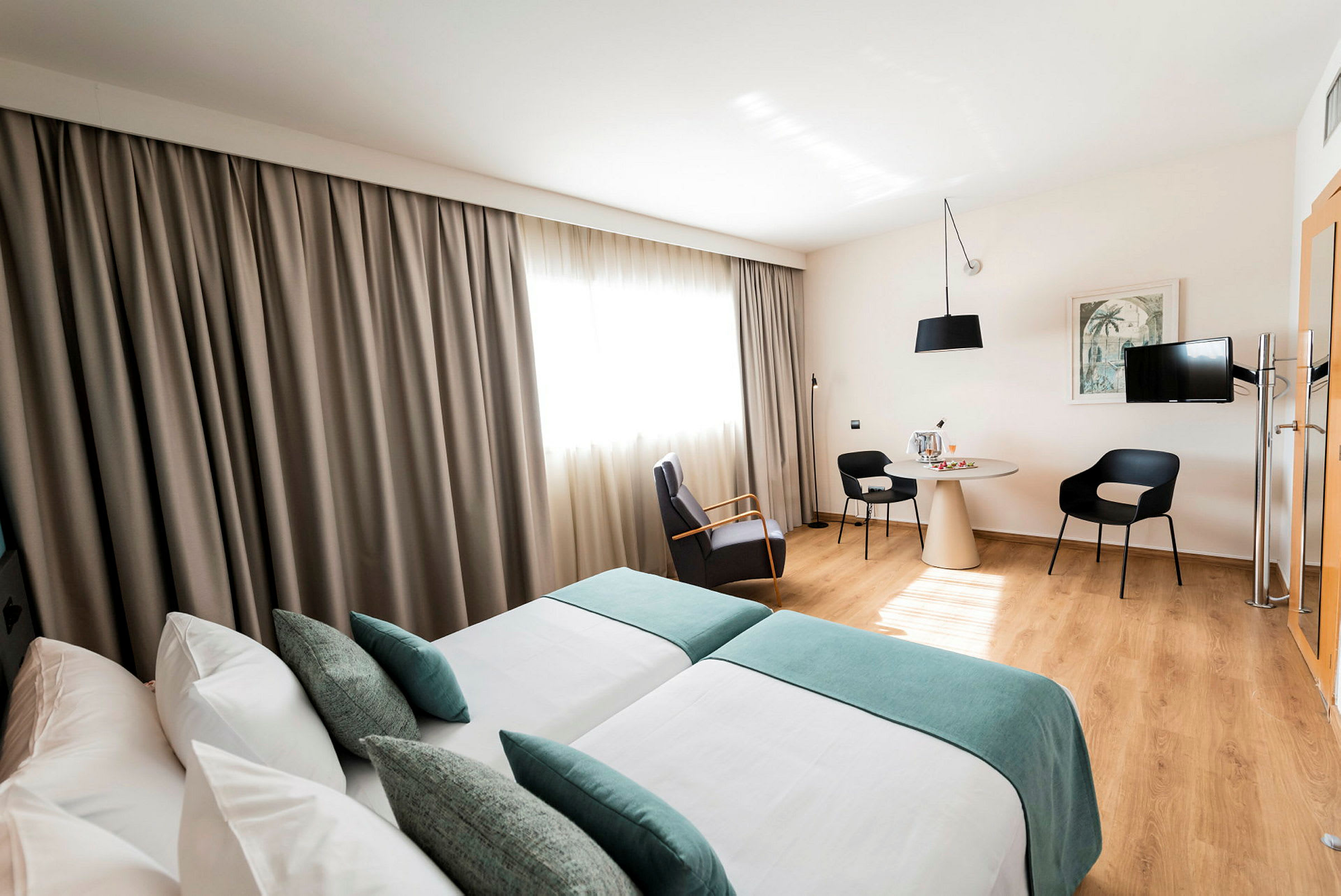 Ett ljust hotellrum med två enkelsängar, sittgrupp och bord. (AI-genererad text)
