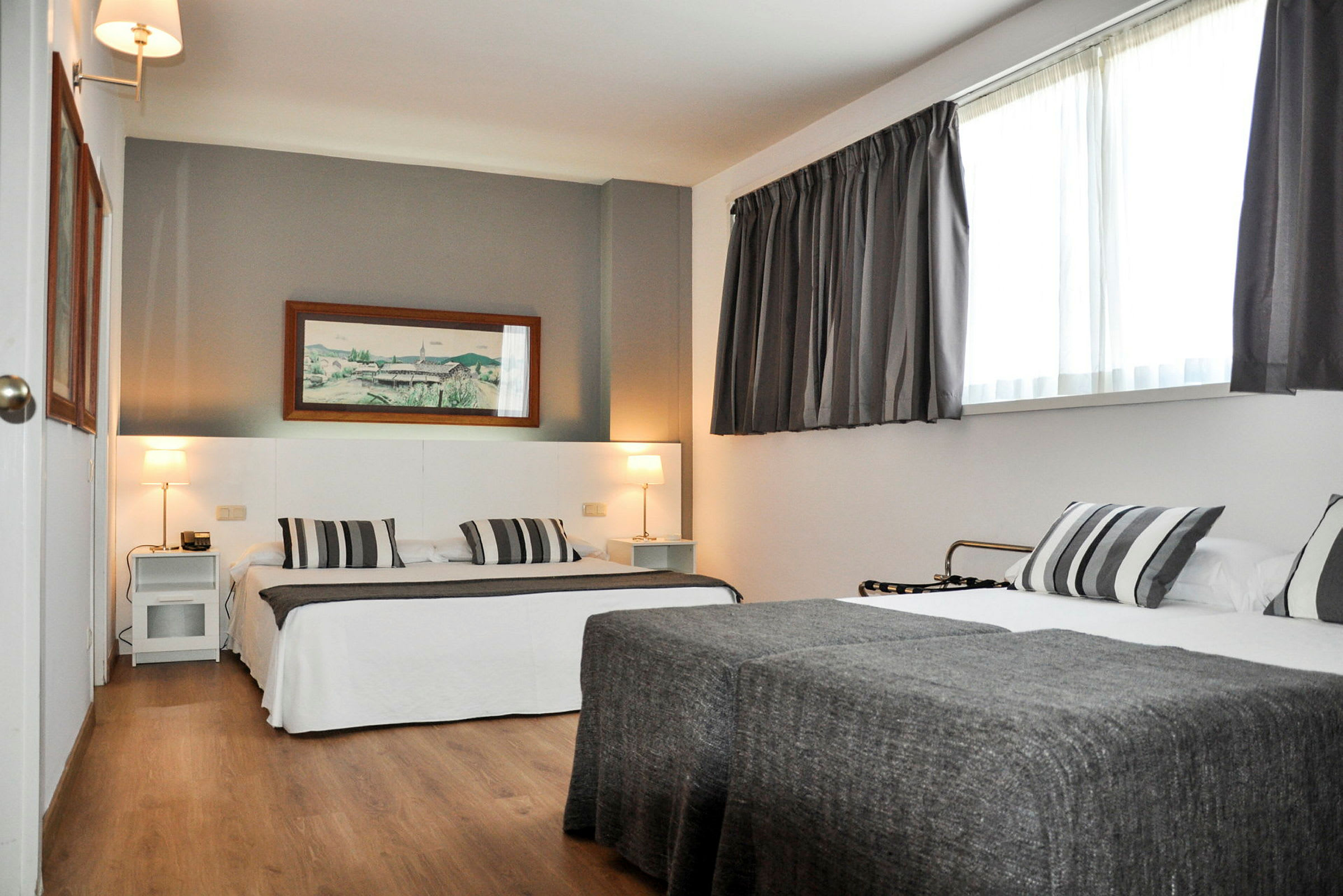 Ett hotellrum med två sängar, grå sängkläder och en väggmålning ovanför den ena sängen. (AI-genererad text)