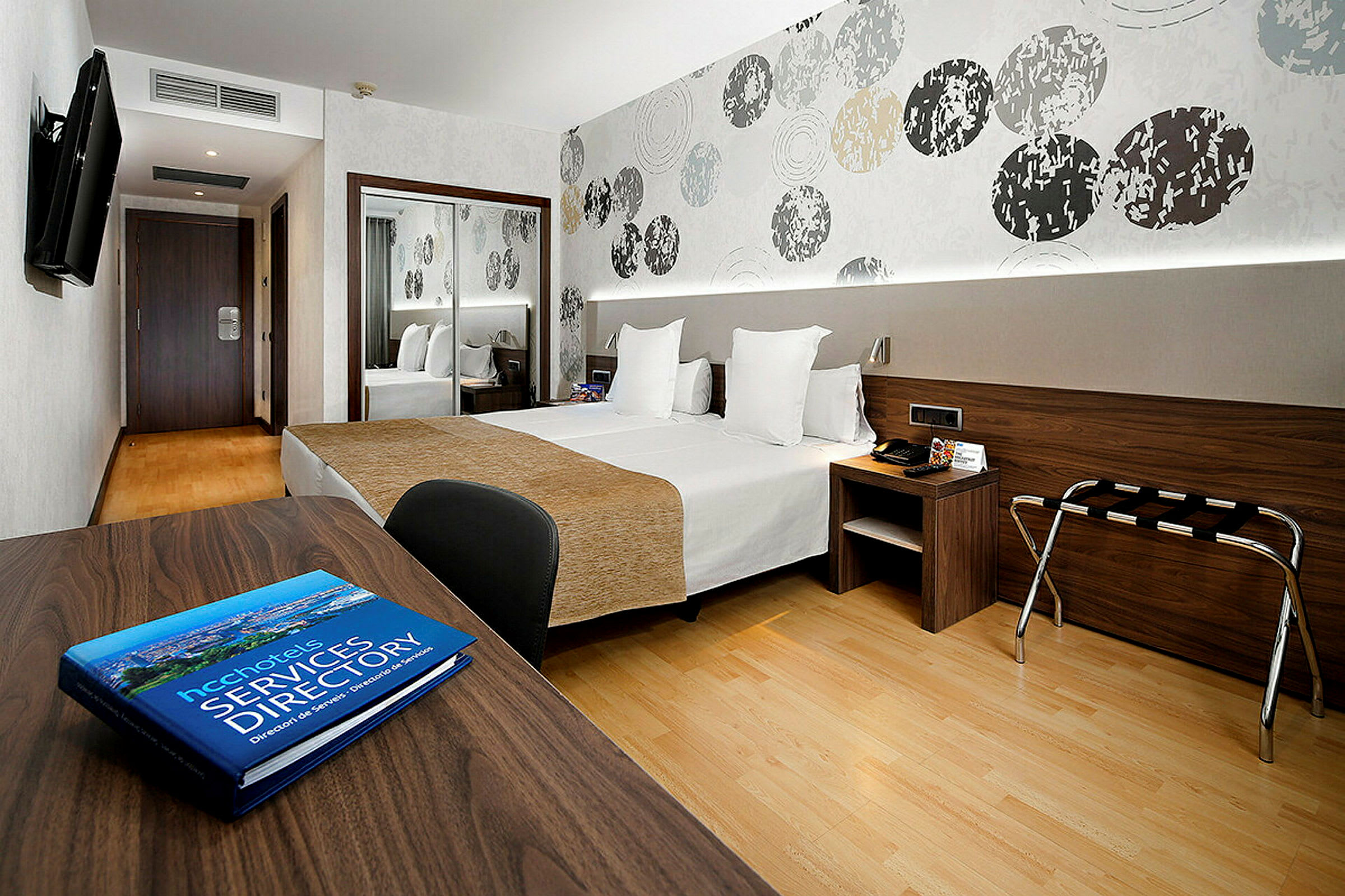 Ett modernt hotellrum med två sängar, ett skrivbord och en abstrakt dekorerad vägg. (AI-genererad text)