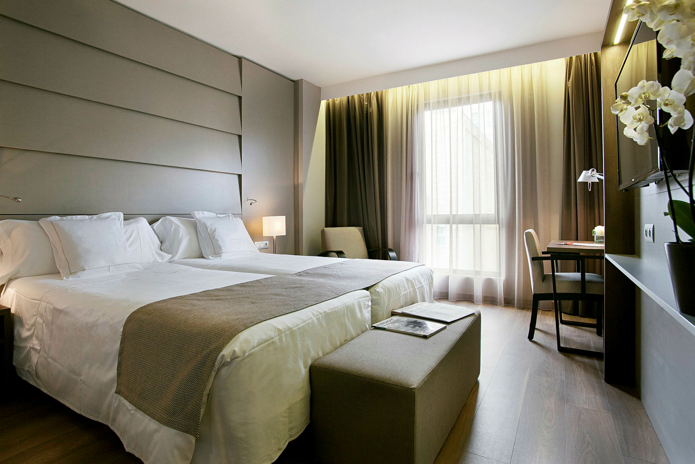 Ett hotellrum med två sängar, skrivbord och stora fönster. (AI-genererad text)