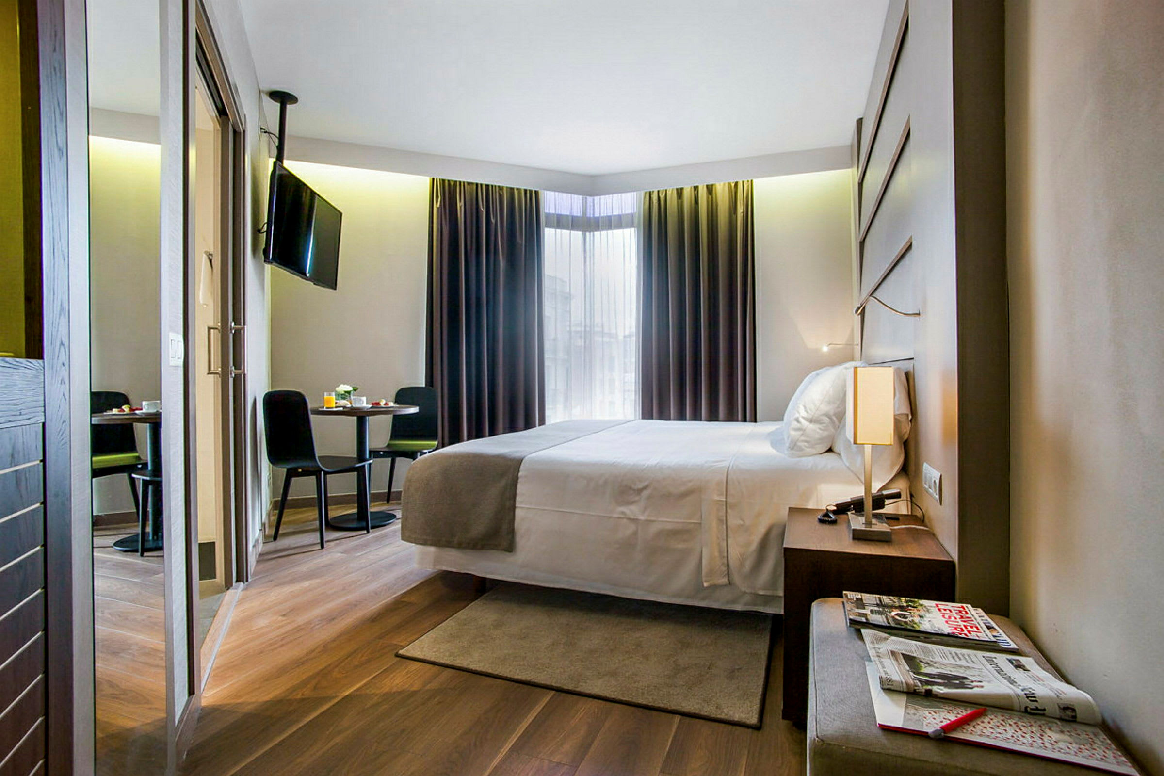 Ett modernt hotellrum med en dubbelsäng, träparkettgolv, ett litet bord med två stolar och en väggmonterad TV. (AI-genererad text)