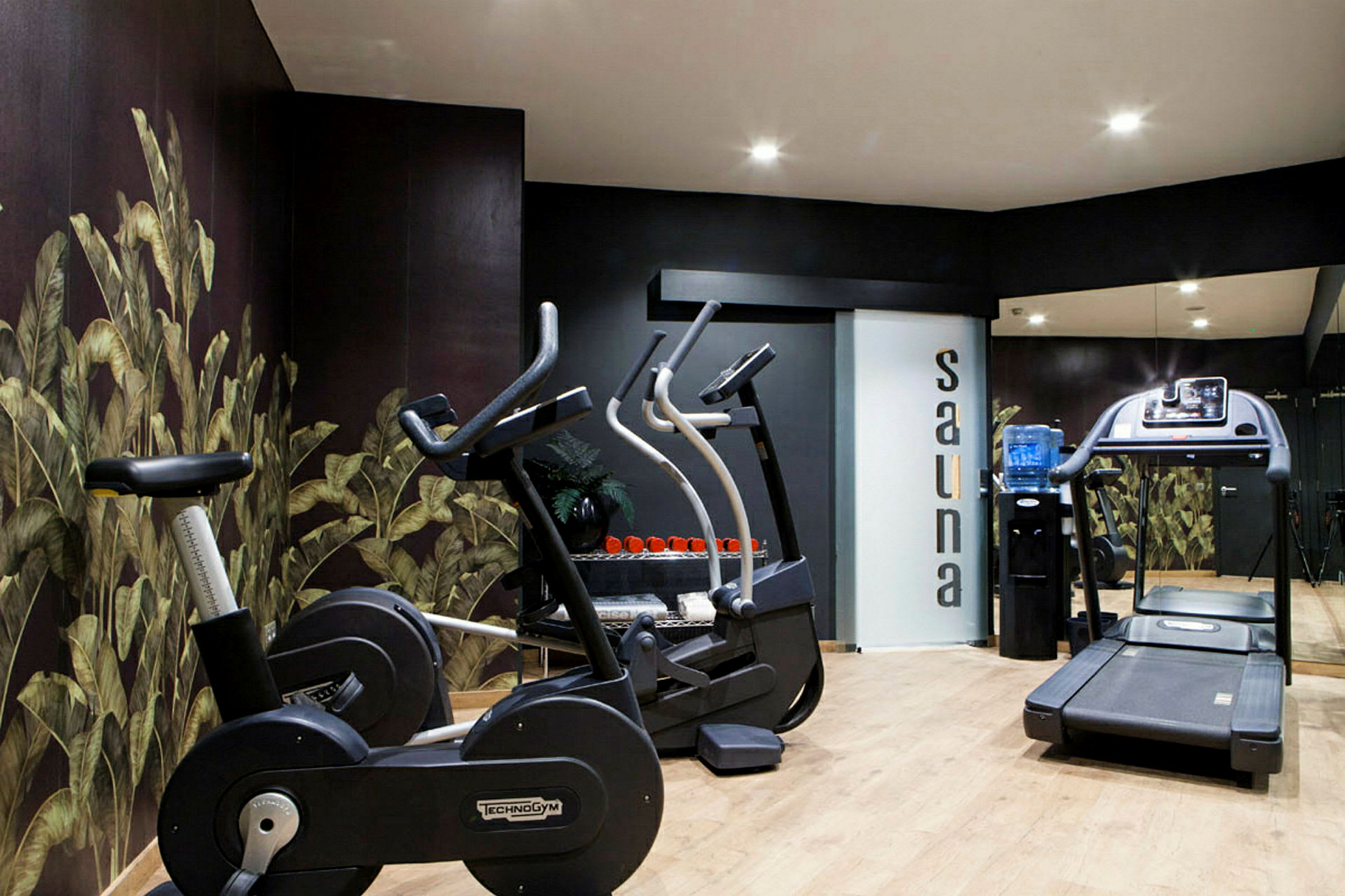 Ett gym med träningscyklar och ett löpband, samt en dörr med texten 'sauna'. (AI-genererad text)