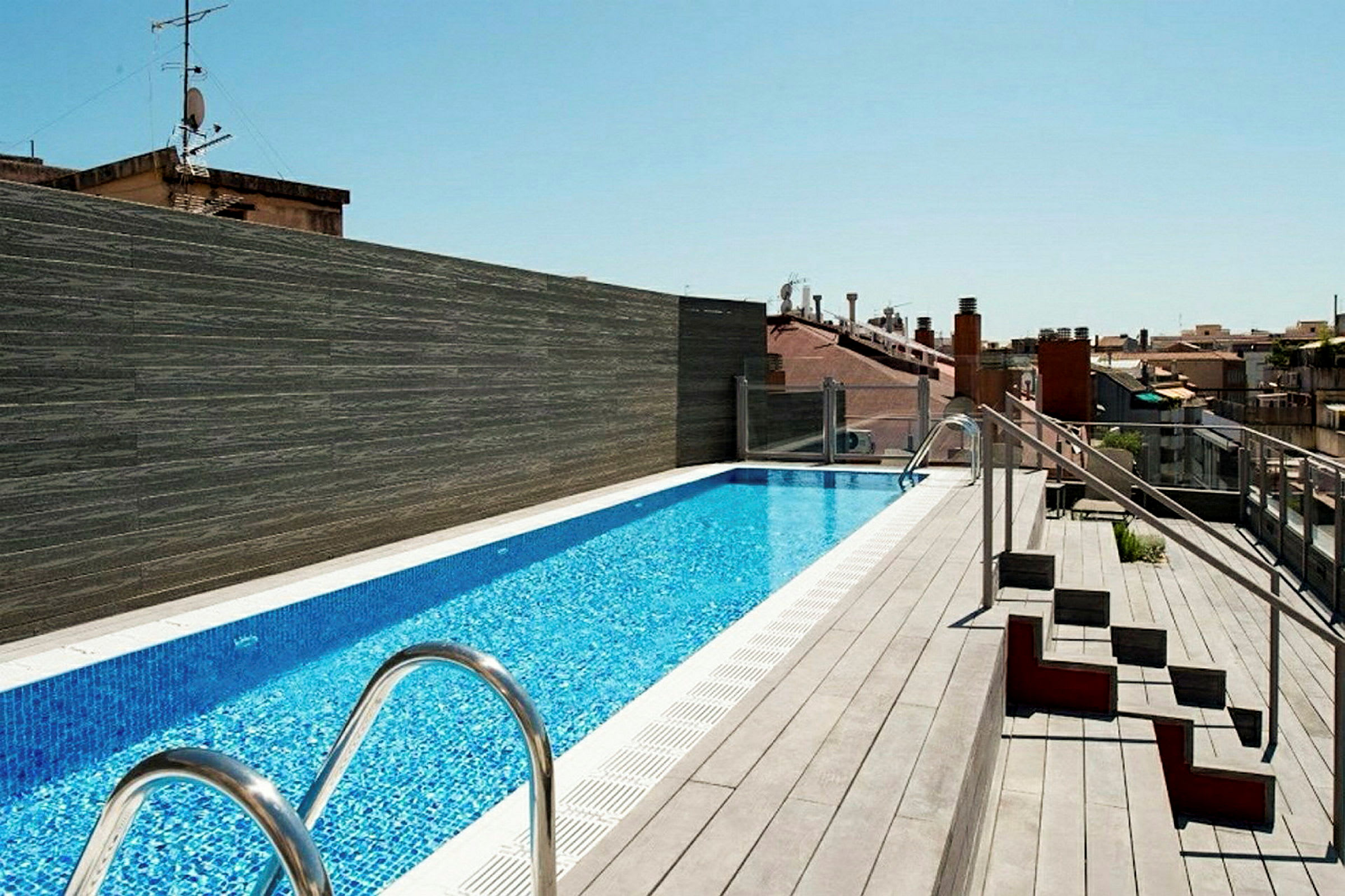 En takterrass med en lång pool omgiven av trädäck och några sittplatser på sidan. (AI-genererad text)