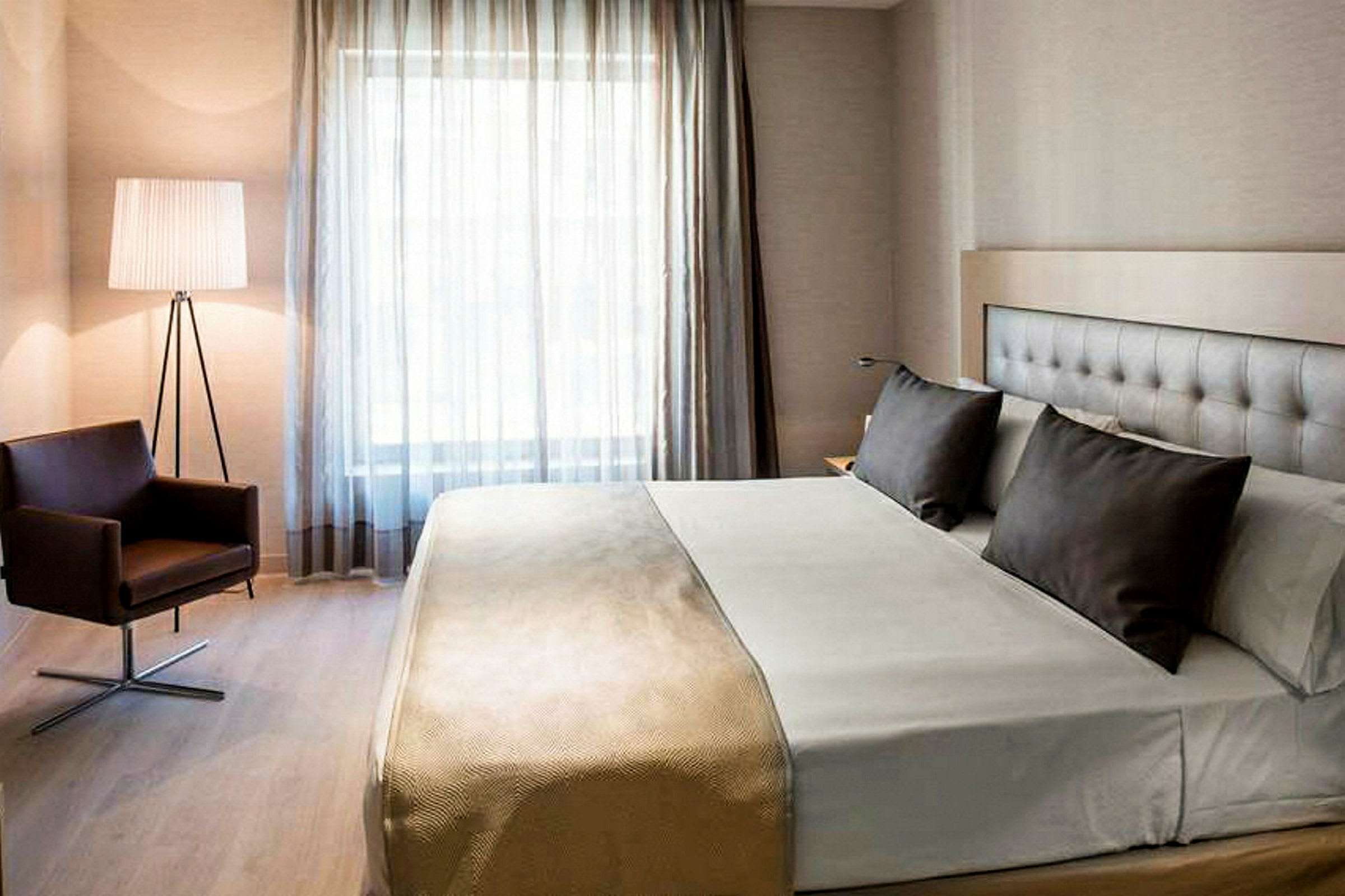 Ett hotellrum med en stor säng, två kuddar och en stol vid sidan. (AI-genererad text)