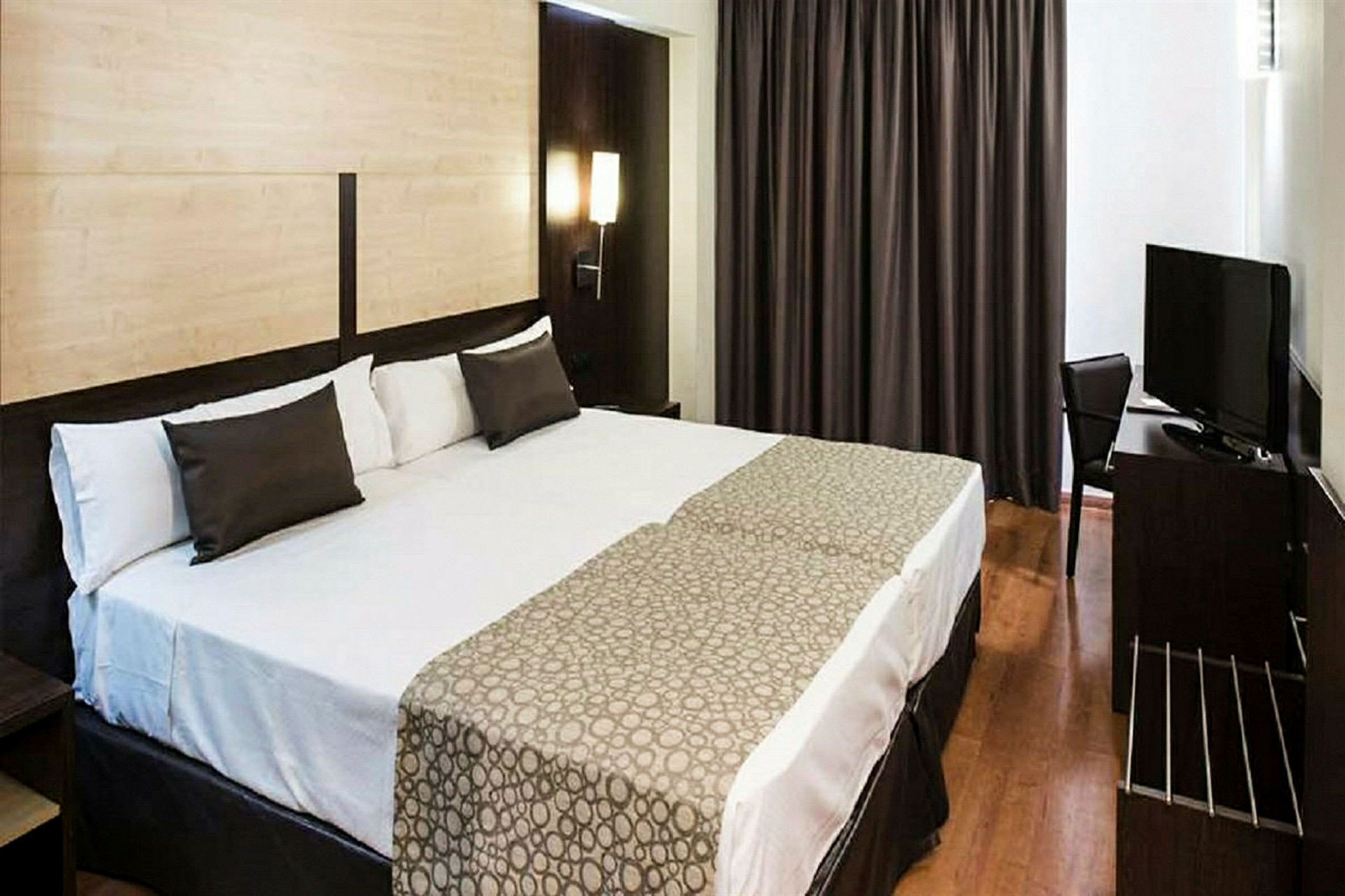 Hotellrum med en stor säng och en TV på skrivbordet bredvid. (AI-genererad text)