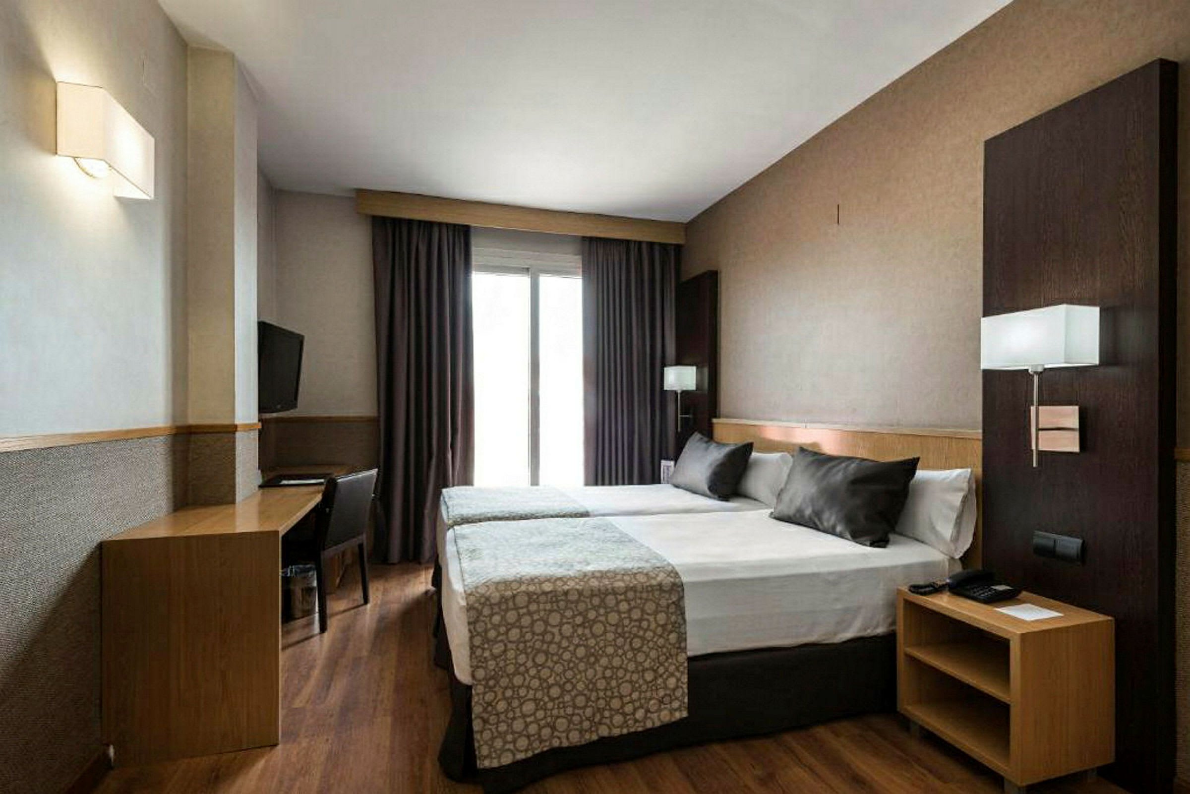 Ett hotellrum med två enkelsängar som står ihop, ett skrivbord med stol och en väggmonterad TV. (AI-genererad text)