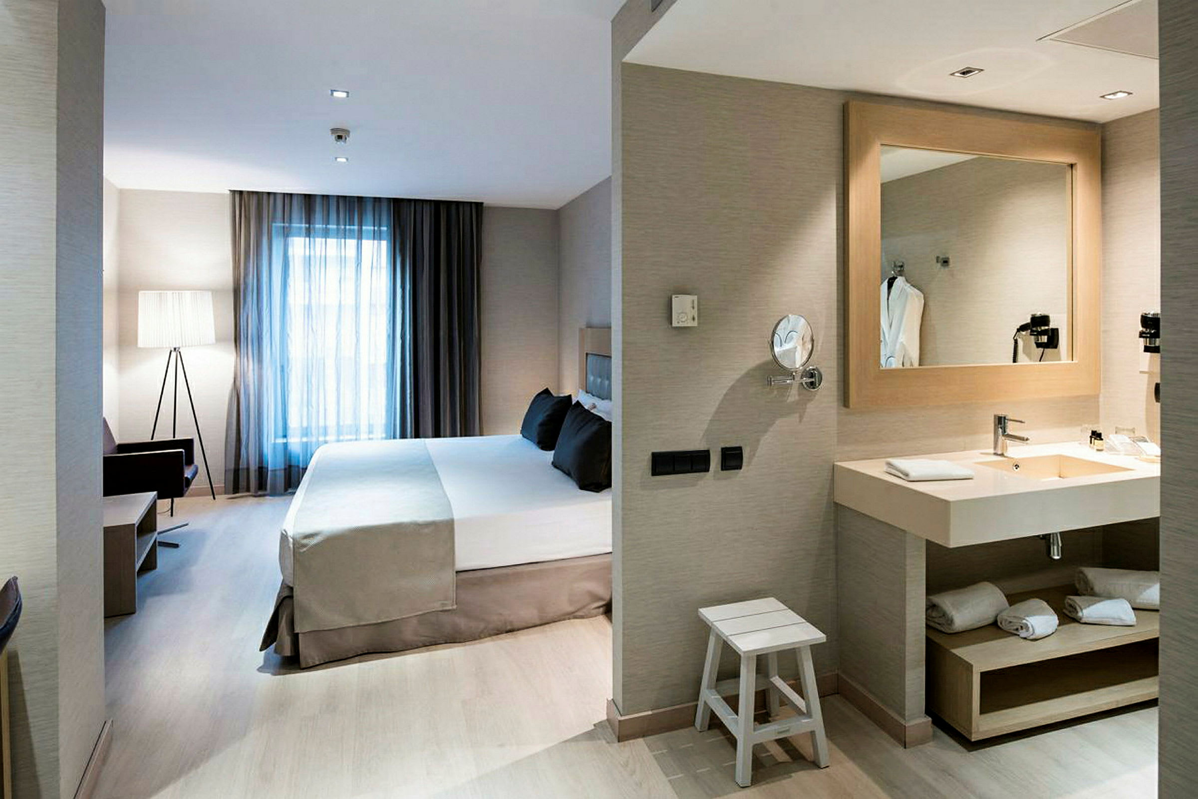 Bild av ett hotellrum med en stor säng, fönster med gardiner, sittplats samt en välkomnande badrumsmiljö. (AI-genererad text)