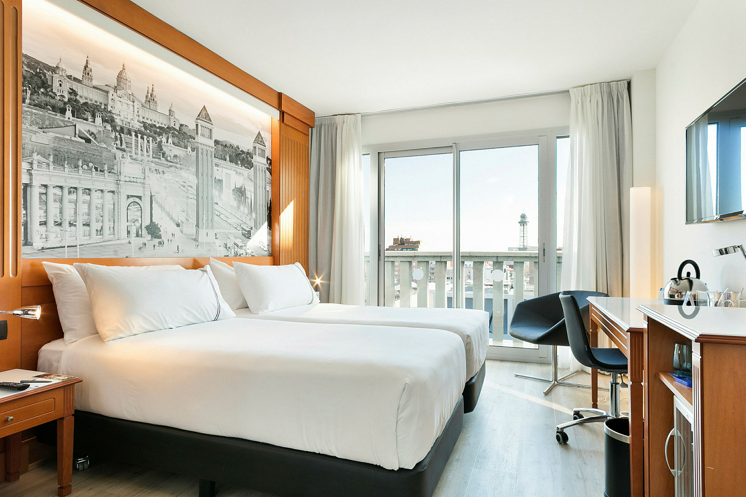 Hotellrum med två enkelsängar, en arbetsyta, och ett fönster med balkongutsikt. (AI-genererad text)