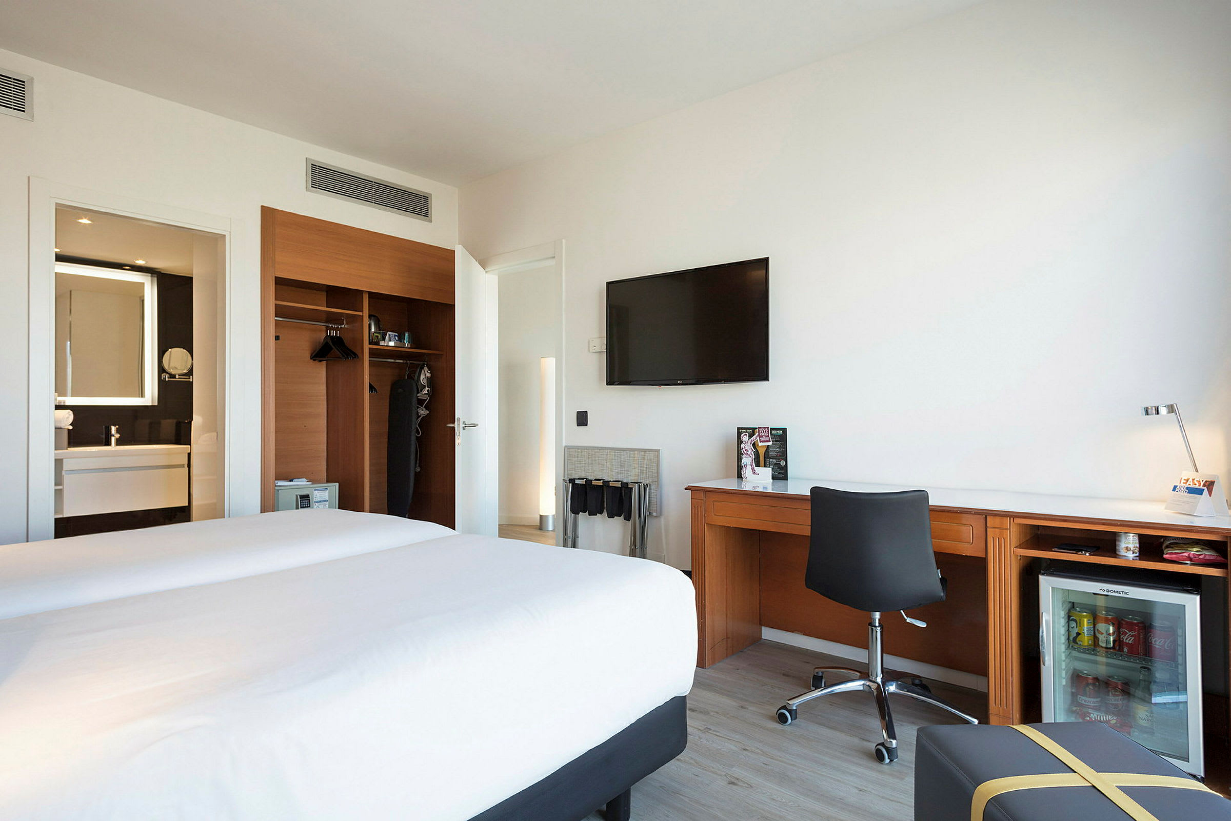 Hotellrum med två sängar, en skrivbordsyta och en garderob samt badrum i bakgrunden. (AI-genererad text)