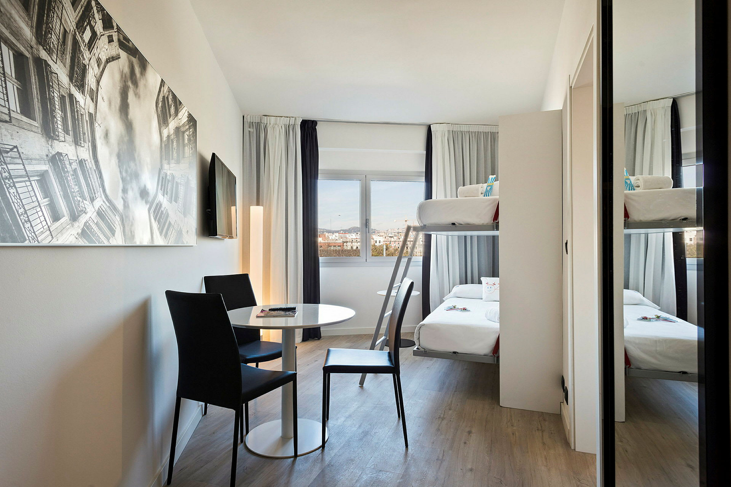 Ett modernt hotellrum med våningssäng, bord och två stolar samt en stor väggbild. (AI-genererad text)