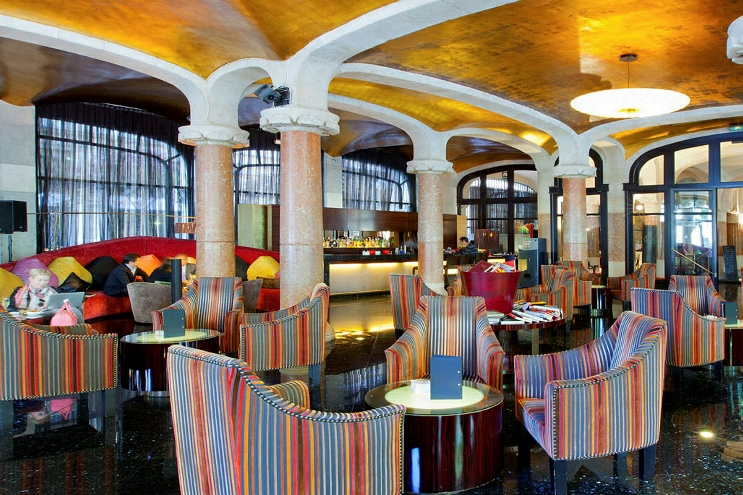 Ett elegant hotellobbyområde med färgglada fåtöljer och runda bord, marmorpelare och ett glänsande golv. (AI-genererad text)