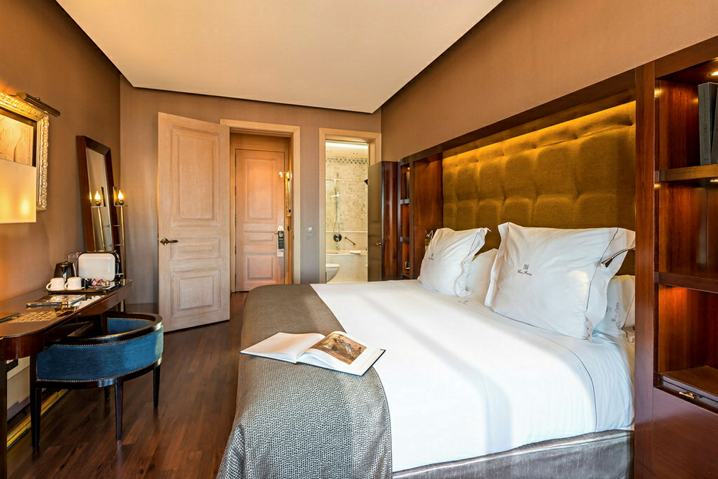 Ett hotellrum med en stor säng bäddad med vita lakan, ett skrivbord med sittplats och en dörr som leder till badrummet. (AI-genererad text)