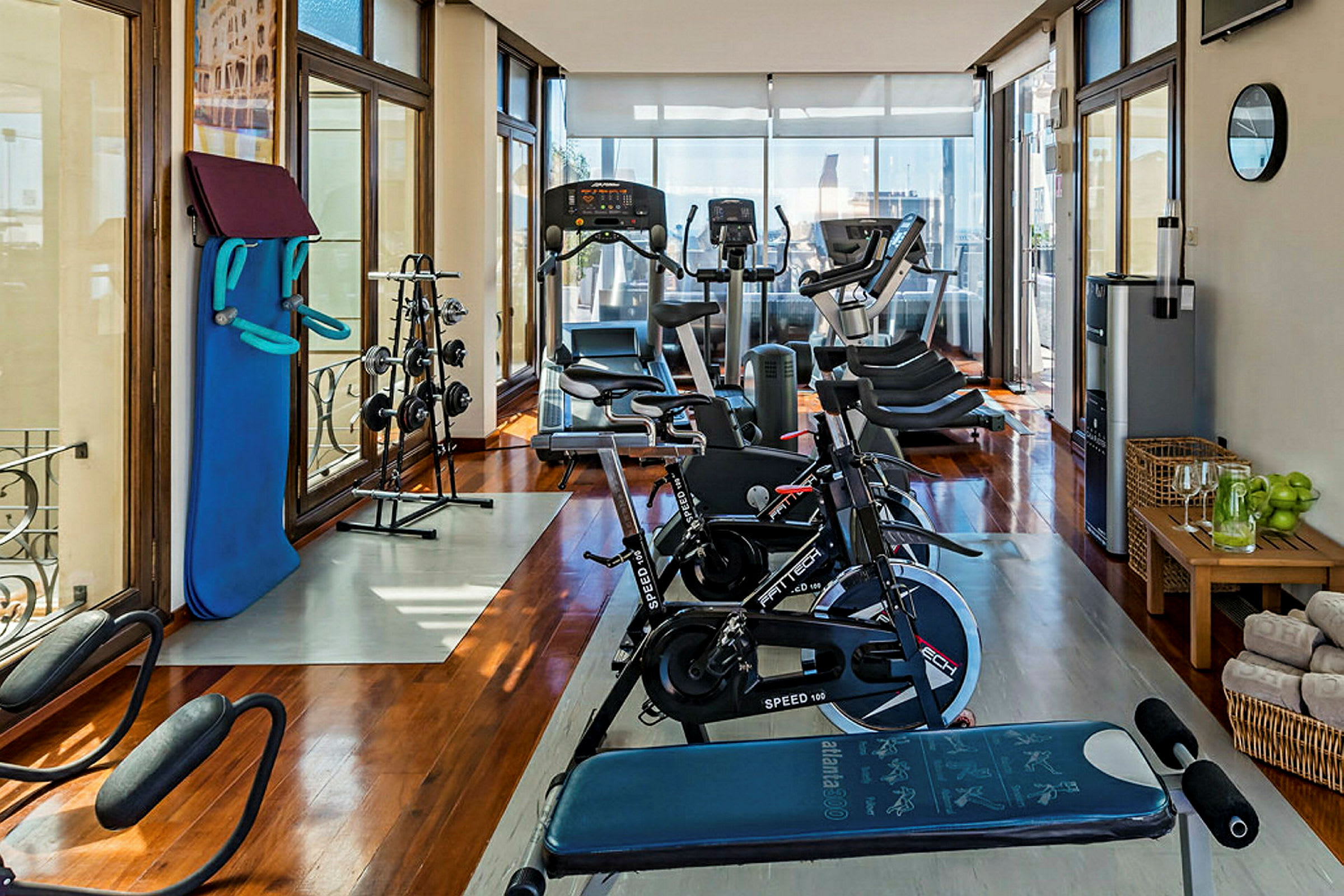 Ett ljust gym med träningsutrustning som inkluderar motionscyklar, löpband, vikter och en bänk, samt stora fönster och bekväma faciliteter. (AI-genererad text)