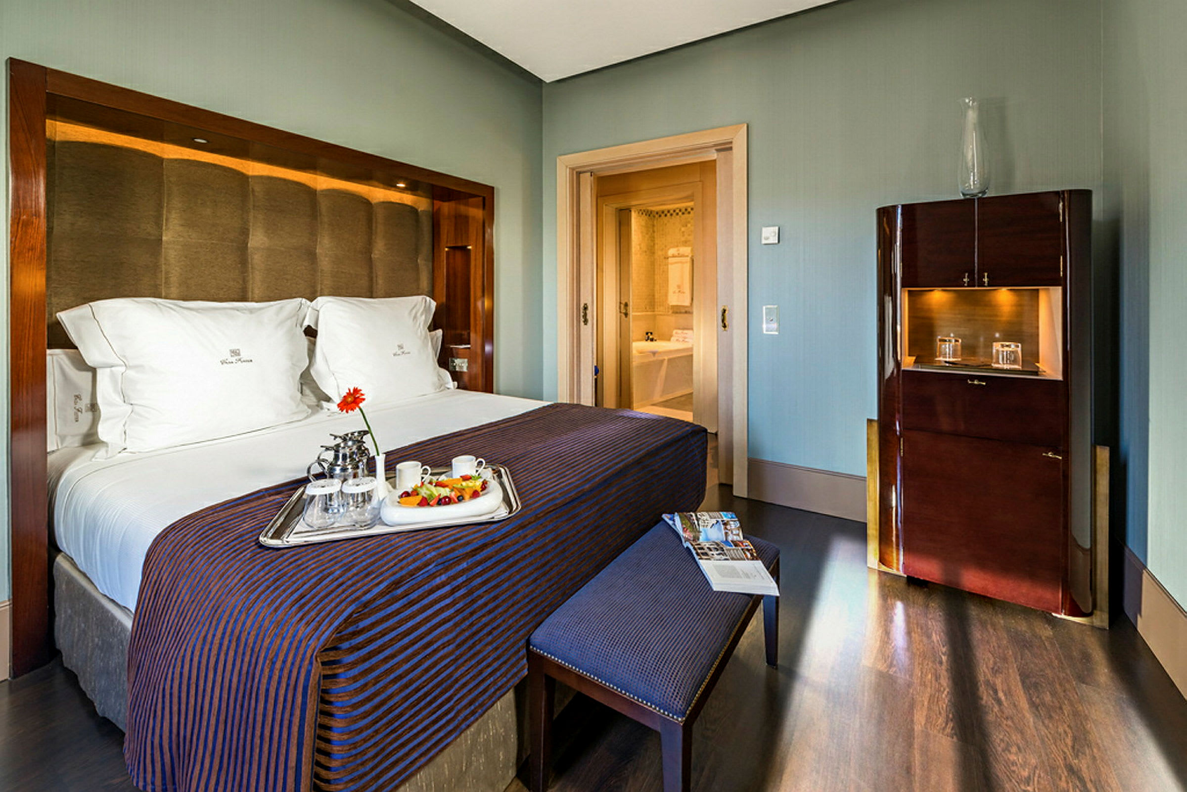 Ett hotellrum med en stor dubbelsäng, frukostbricka på sängen, och öppningen till ett badrum i bakgrunden. (AI-genererad text)
