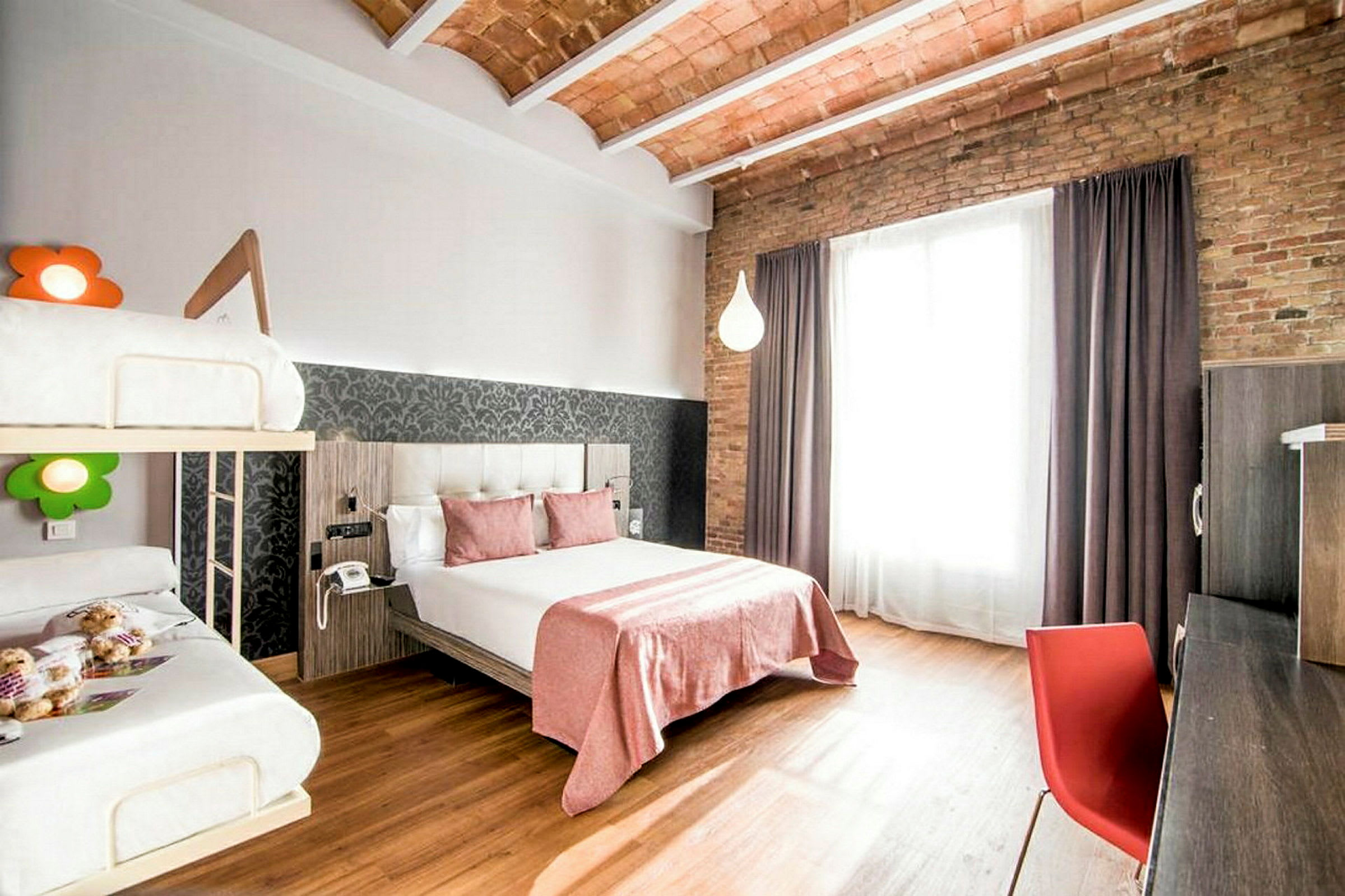 Ett modernt hotellrum med en dubbelsäng, våningssäng, skrivbord och stora fönster med gardiner. (AI-genererad text)