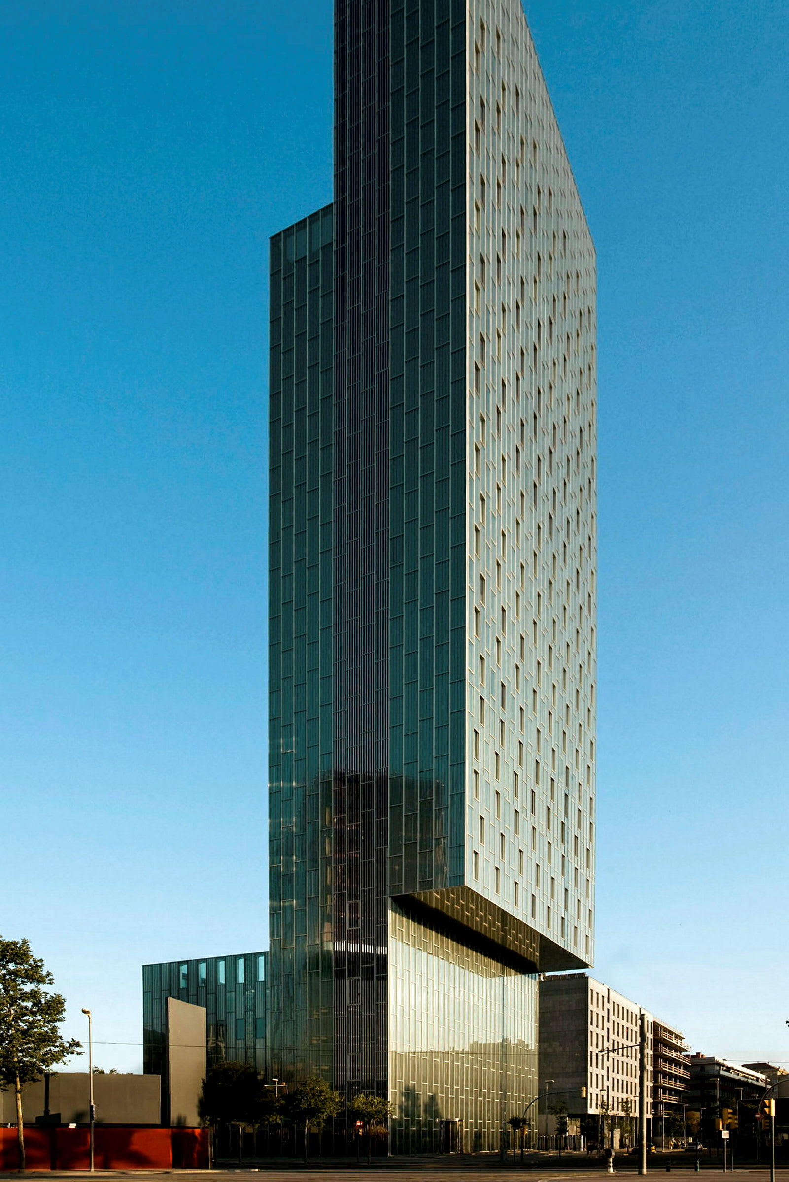 Hög byggnad med modern arkitektur omgiven av blå himmel och urbana byggnader. (AI-genererad text)