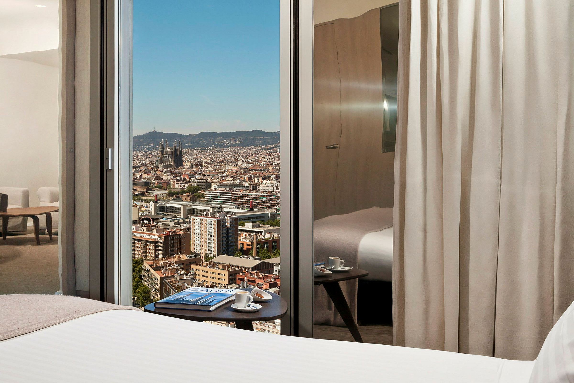 Hotellrum med utsikt över en stad genom glasfönster. (AI-genererad text)