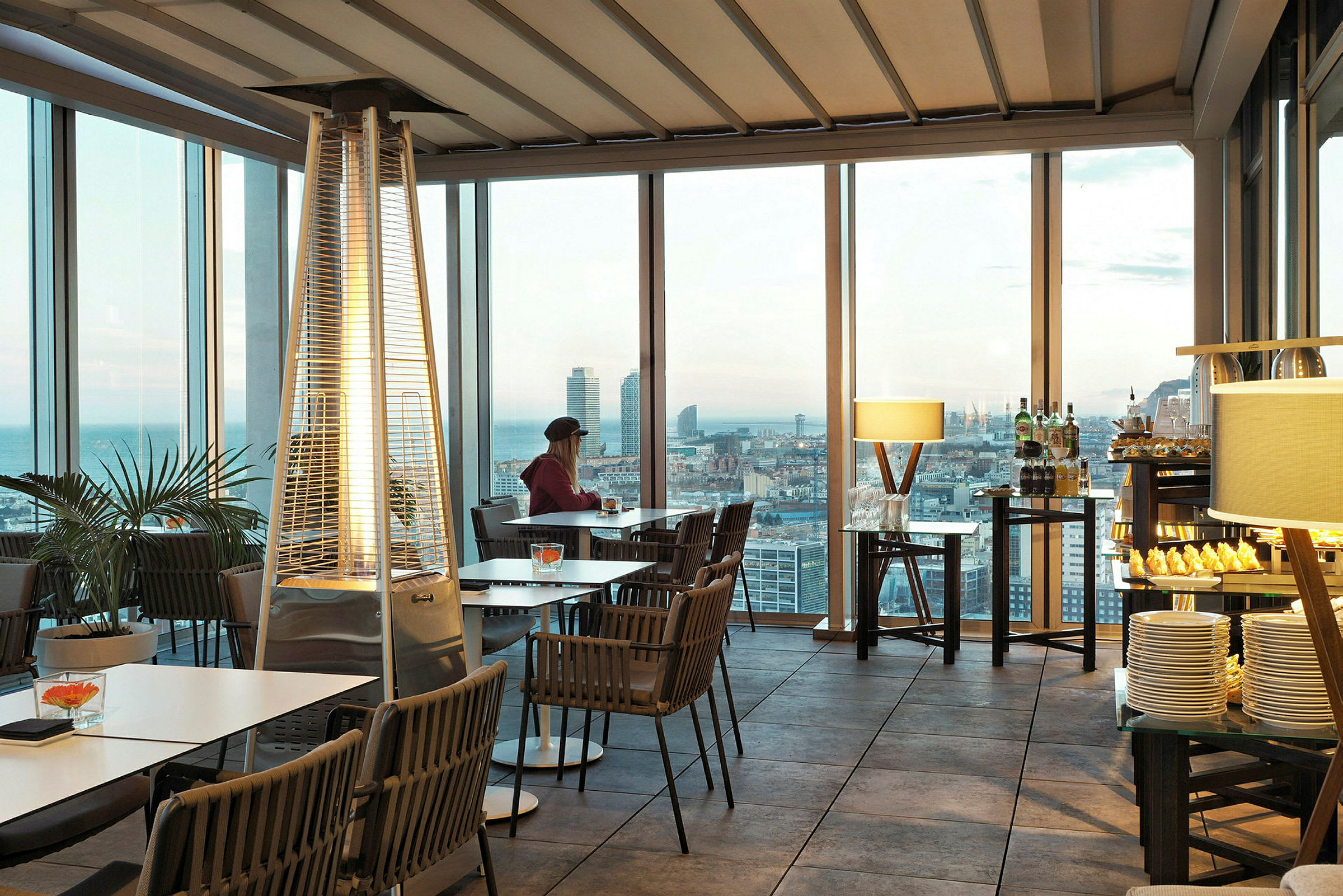 Person som sitter vid ett bord i en restaurang med stora fönster och utsikt över staden. (AI-genererad text)