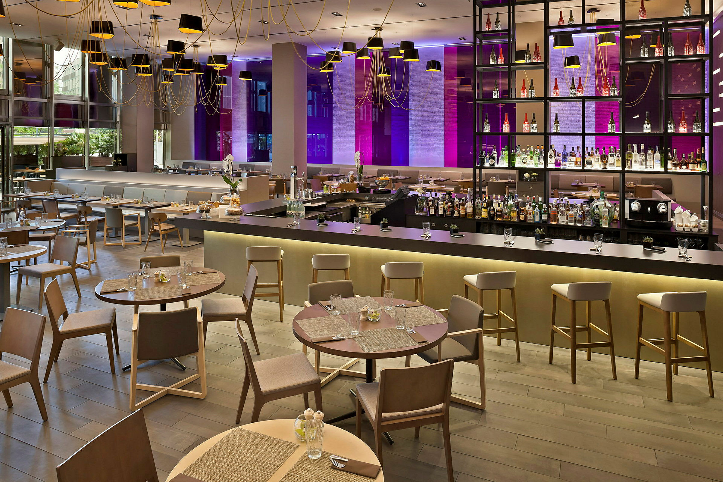 Bild av en modern restaurang med eleganta bord och stolar, en lång bardisk och en dekorativ bakvägg med flaskor samt belysning. (AI-genererad text)