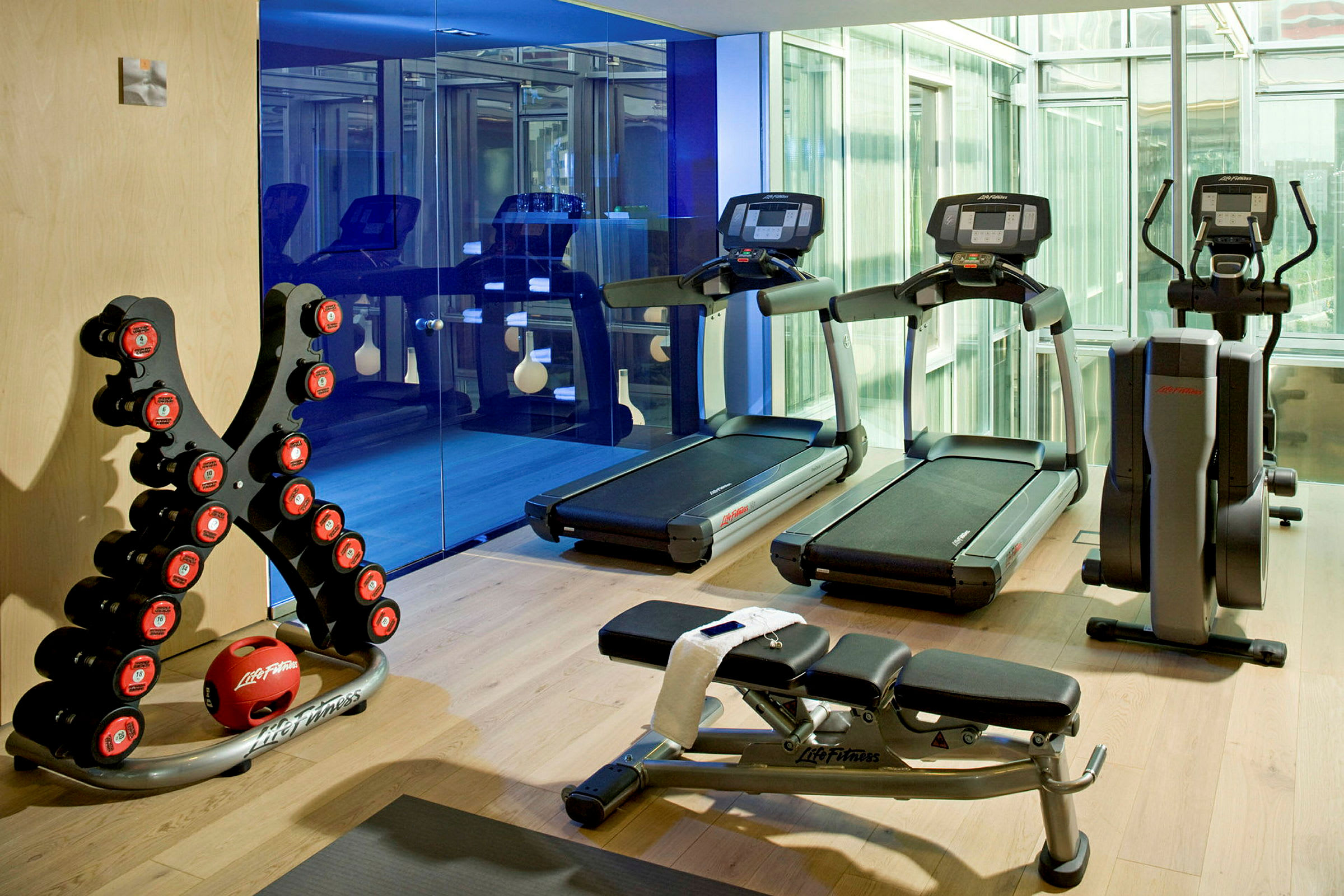 Ett gym med träningsmaskiner, bänkar och fria vikter på trägolv. (AI-genererad text)